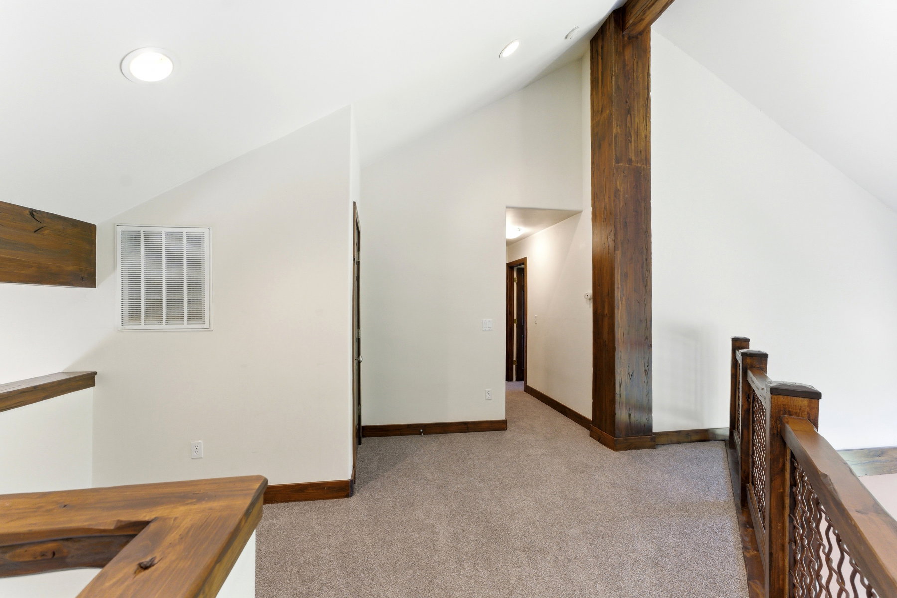 Carpeted upper-level landing featuring vaulted ceilings, recessed lighting, substantial wood structural beams, and a decorative wood railing