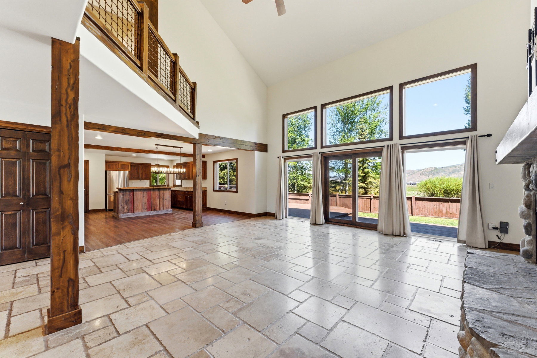 Spacious living area featuring stone tile flooring, a vaulted ceiling, and an exposed wood beam framework