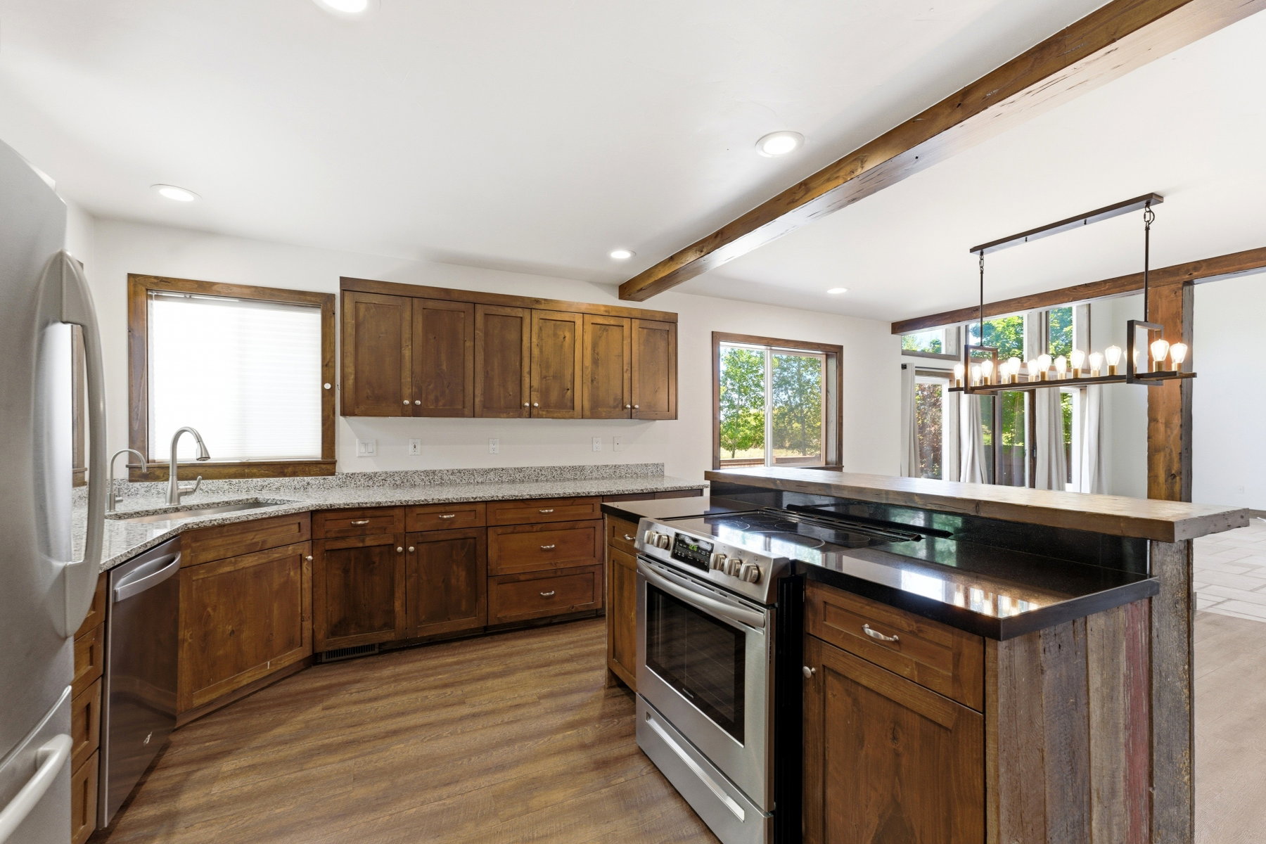 Spacious kitchen featuring wood cabinetry, granite-style countertops, stainless steel appliances, and wood-finish flooring