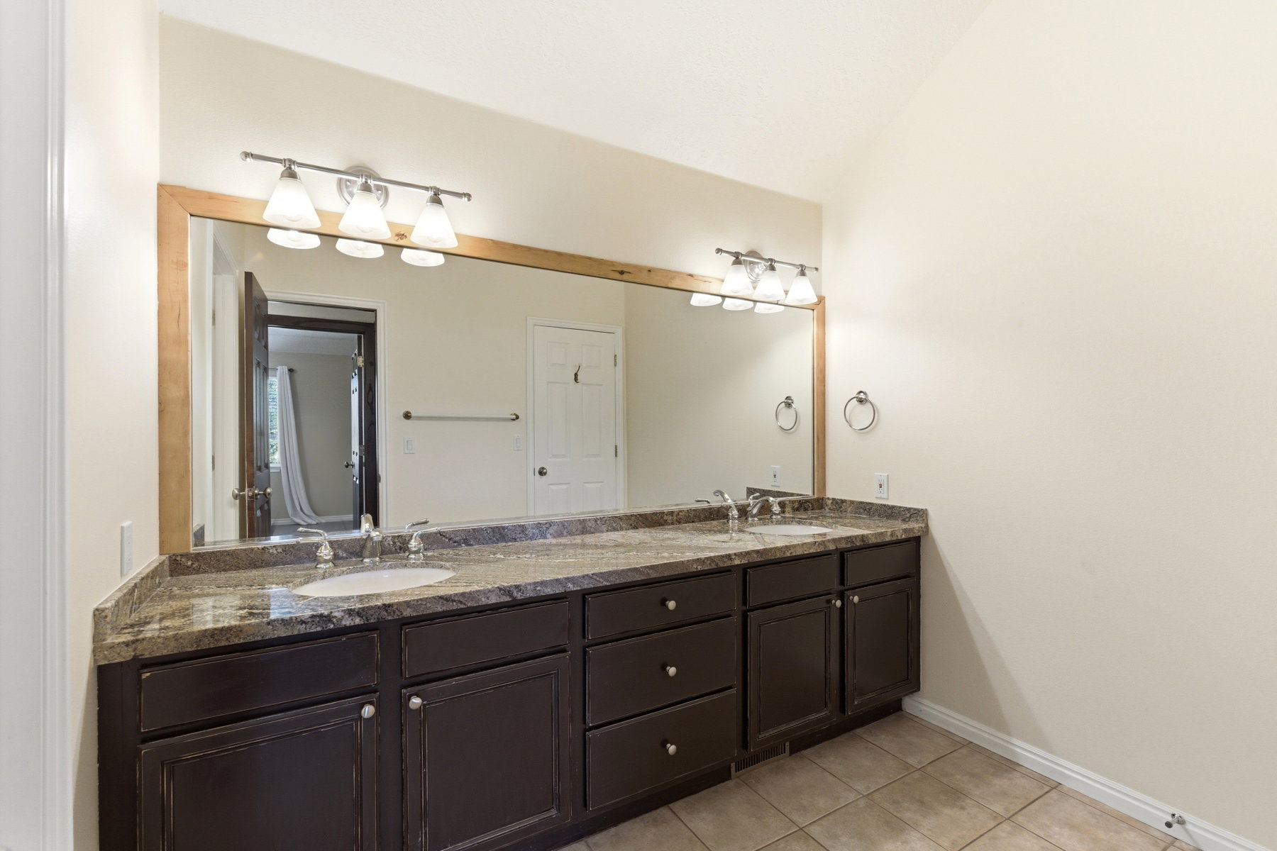 Double vanity with integrated sinks, a wood-framed mirror, and two three-light fixtures
