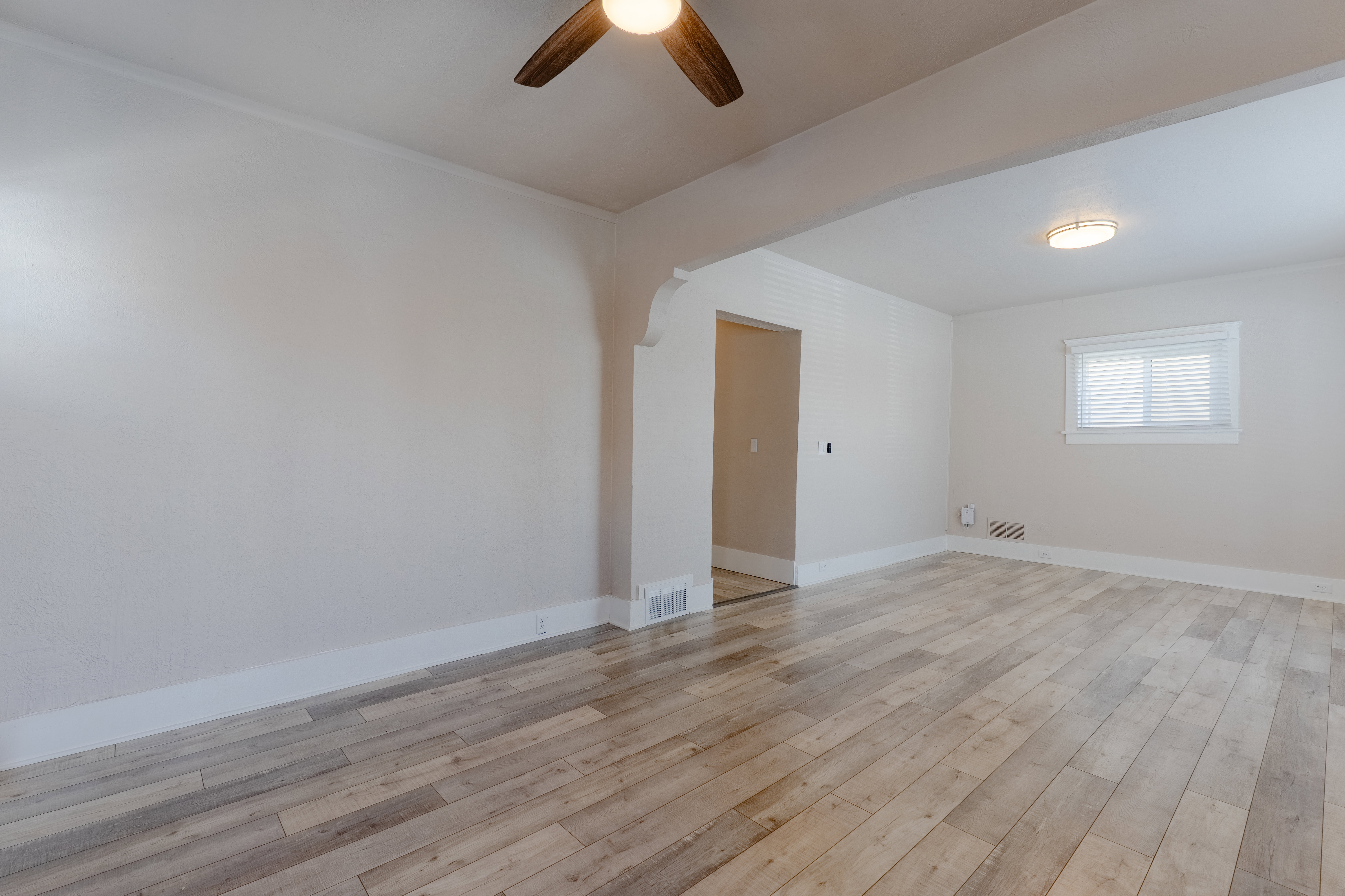 Spacious room featuring wood-finish flooring, light-toned walls, and a ceiling fan with integrated lighting