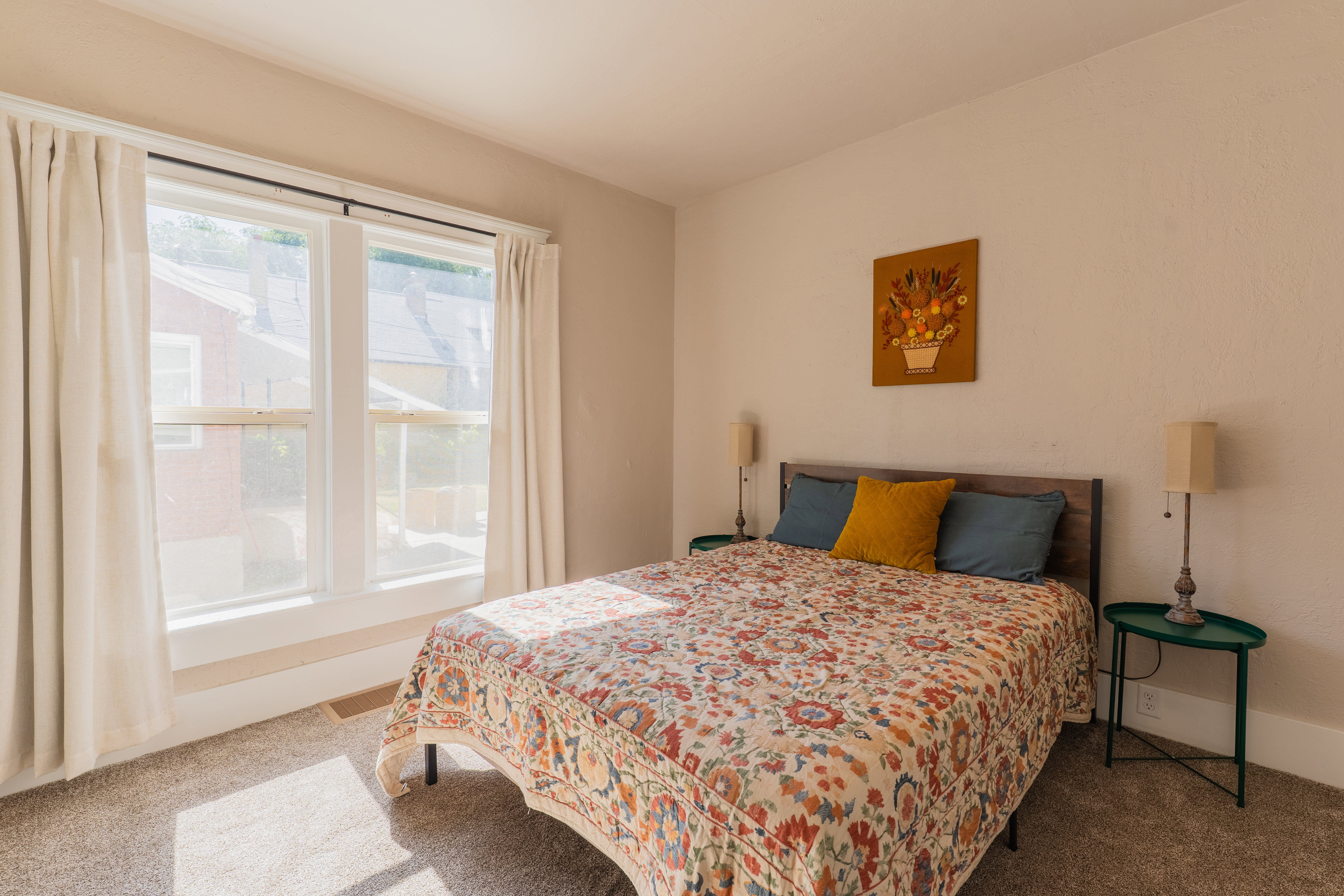 Bedroom space featuring a large double window with white trim, neutral-toned walls, and soft grey carpeting