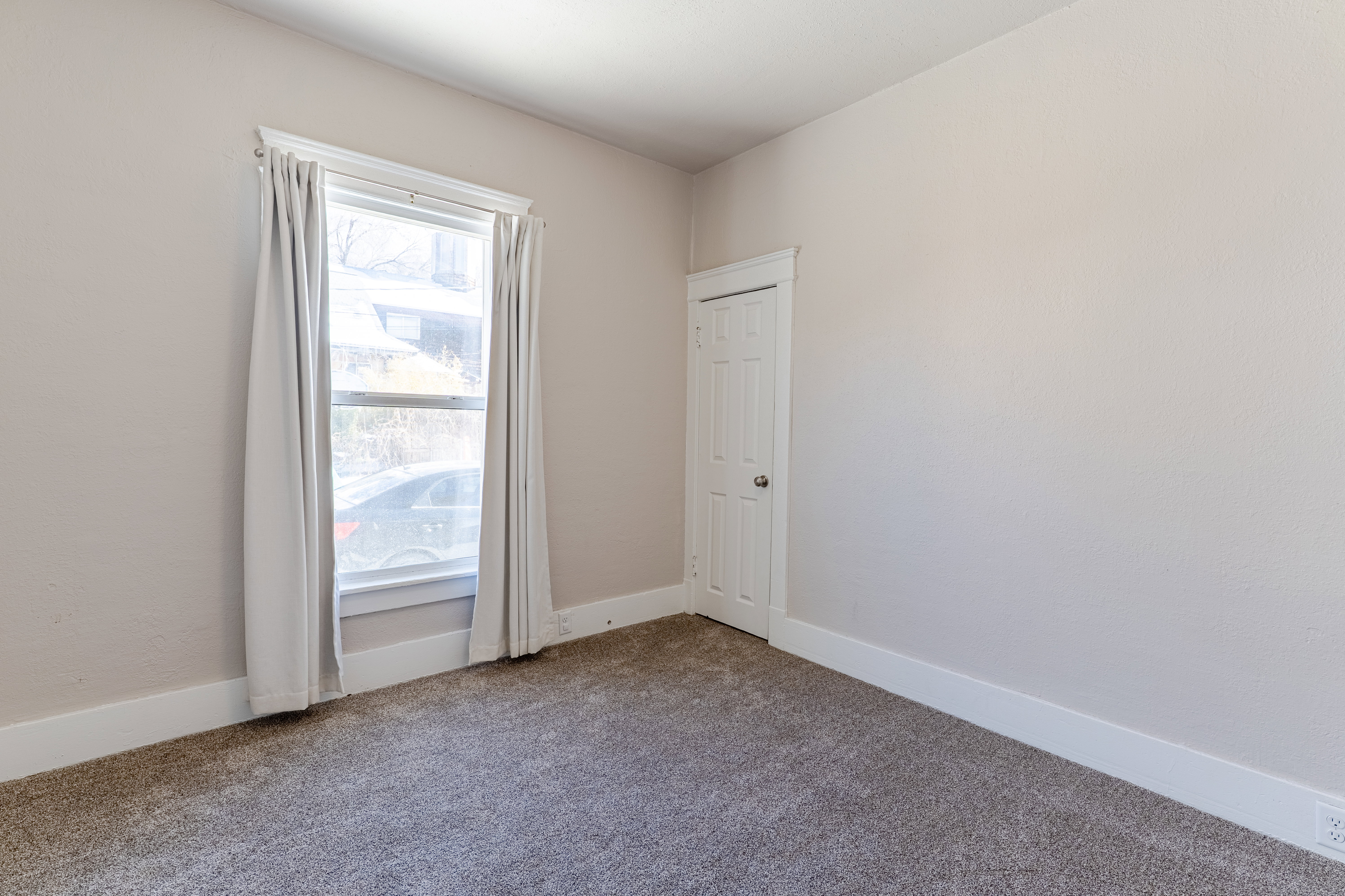 Room featuring neutral painted walls, white trim, gray carpeting, a window with white casing, and a white paneled door