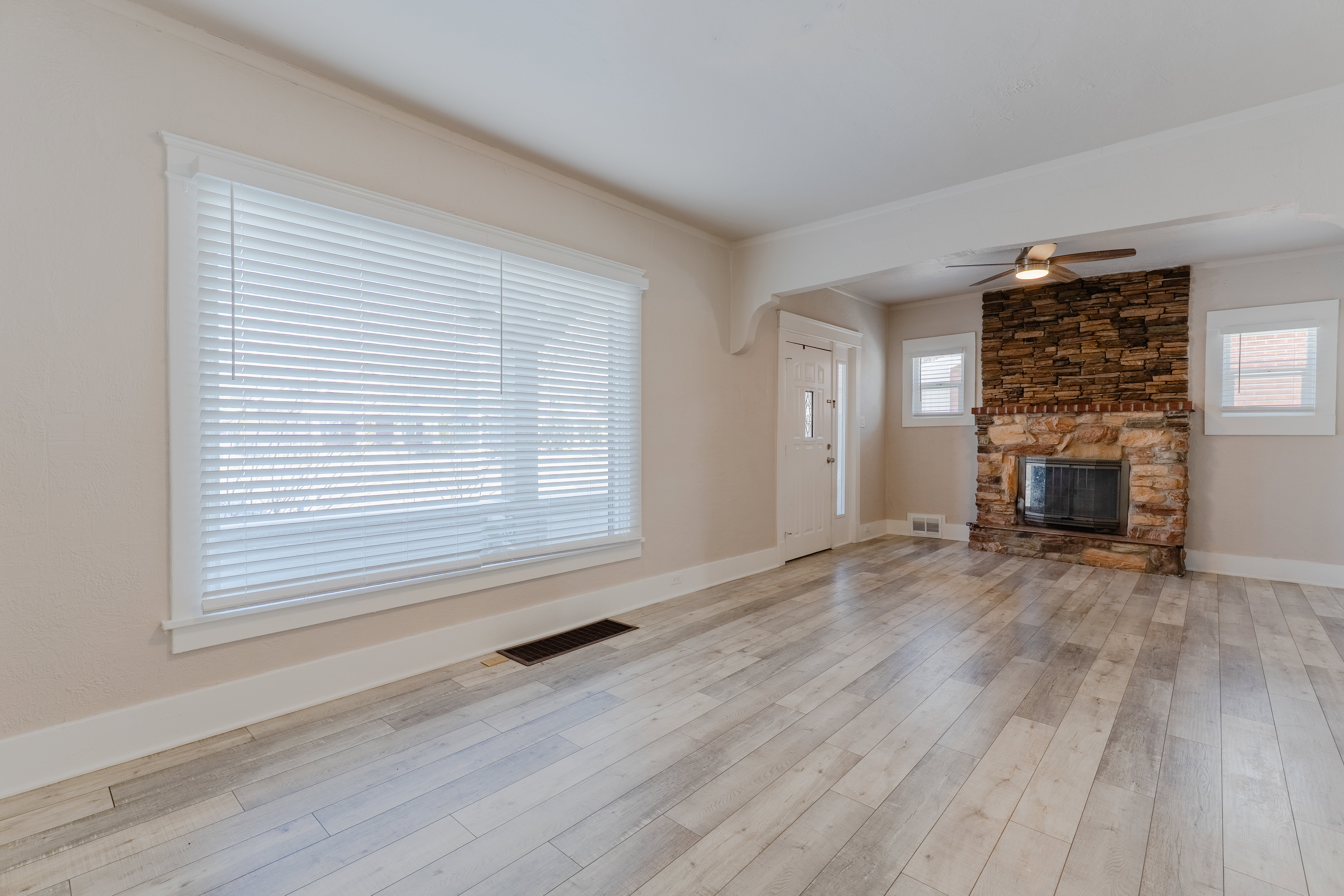Spacious living area featuring light wood-finish flooring, a stone fireplace, and a ceiling fan