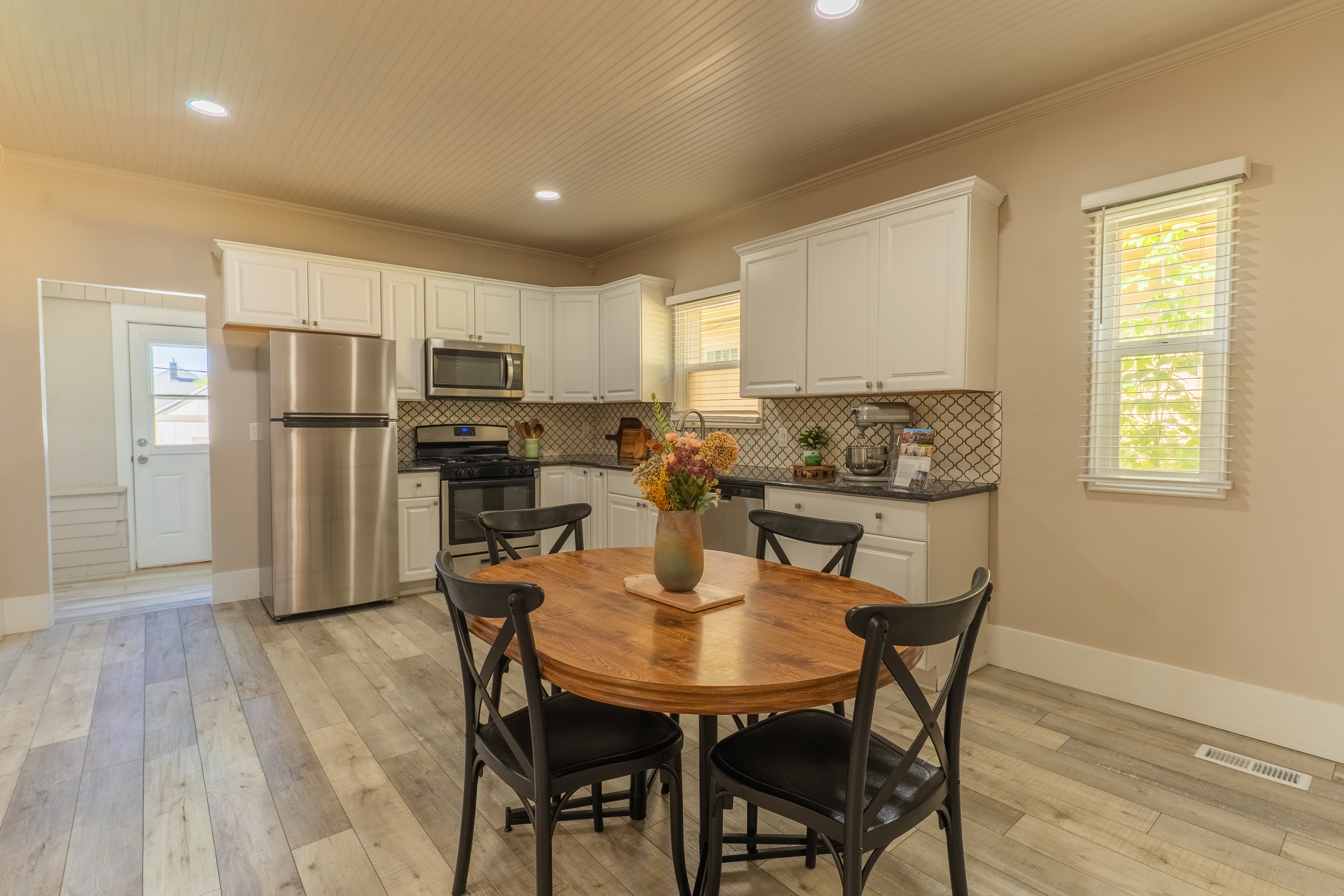 Kitchen area featuring white cabinetry, stainless steel appliances, a geometric tile backsplash, dark countertops, and wood-finish flooring