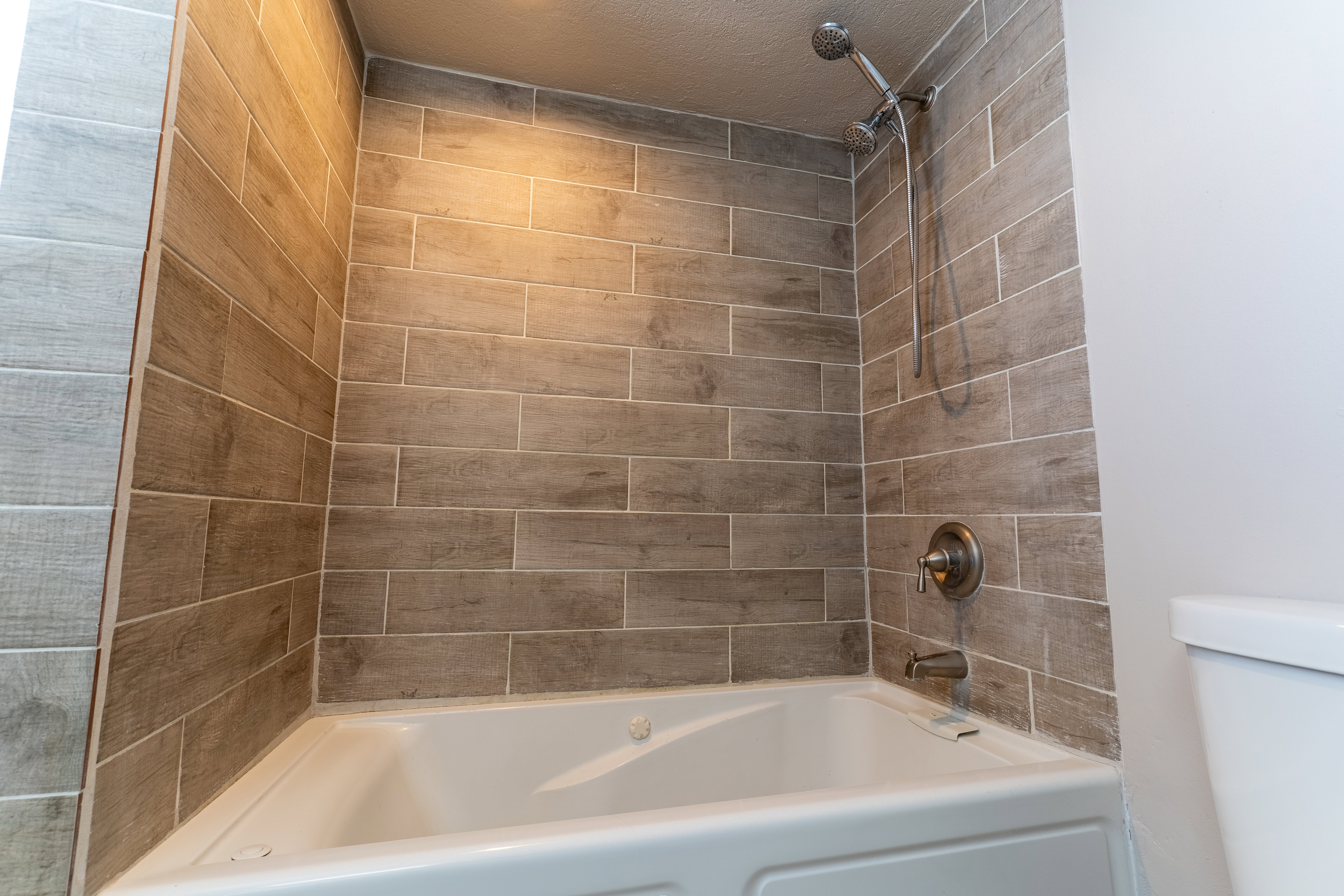 White bathtub with integrated jets, surrounded by wood-finish tile walls