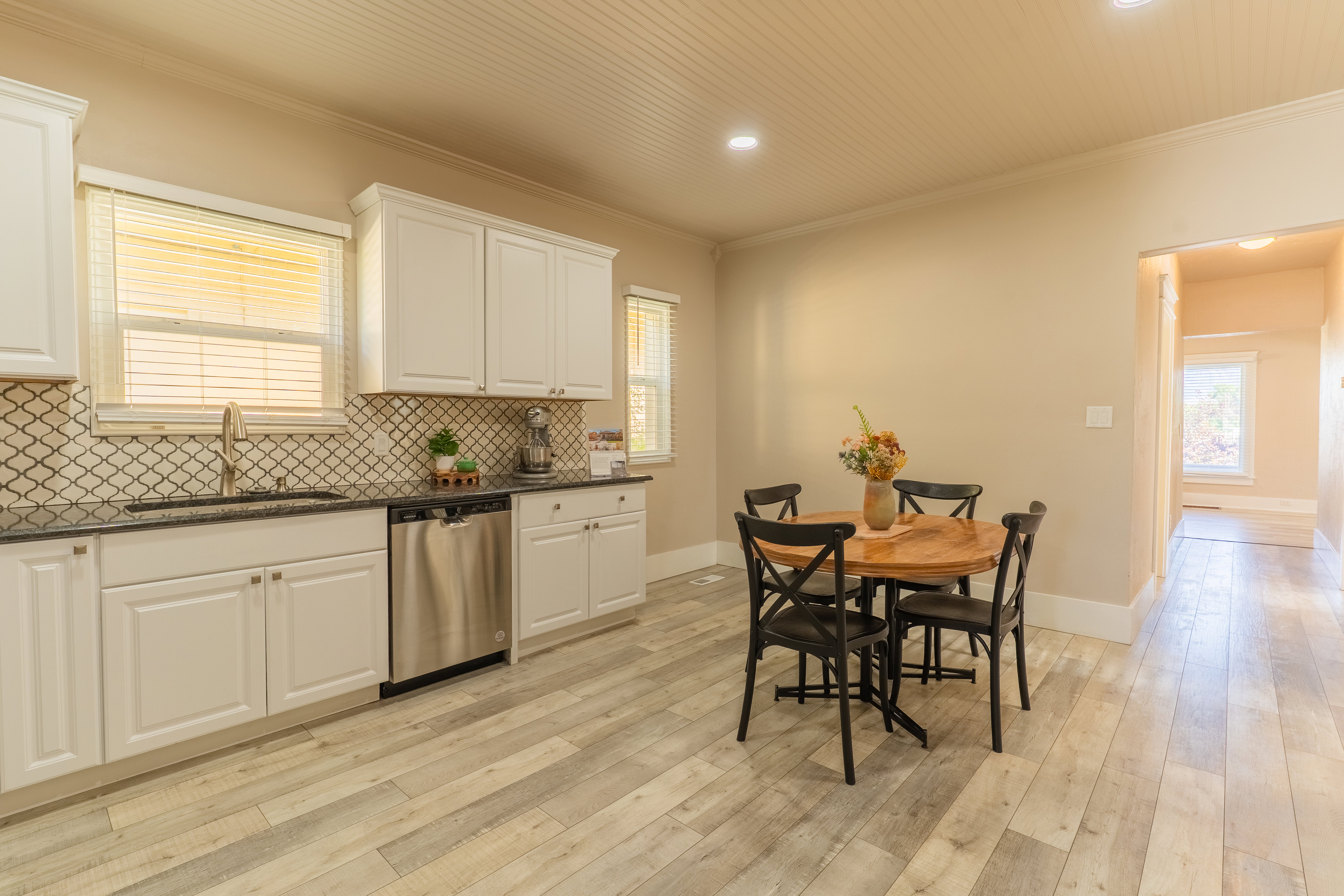 Kitchen featuring white cabinetry, dark countertops, a decorative tile backsplash, stainless steel dishwasher, and wood-finish flooring