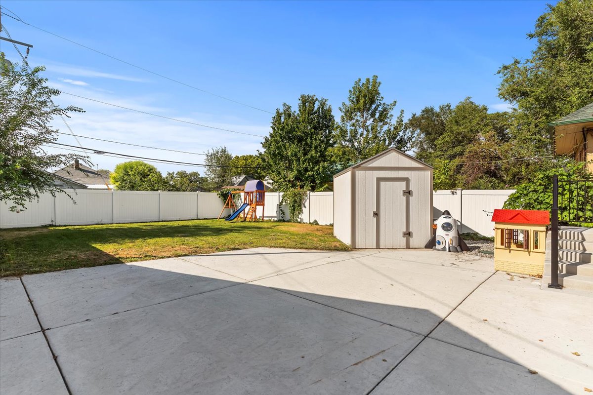 Expansive backyard featuring a large concrete patio, a manicured lawn, a white privacy fence, and a storage shed