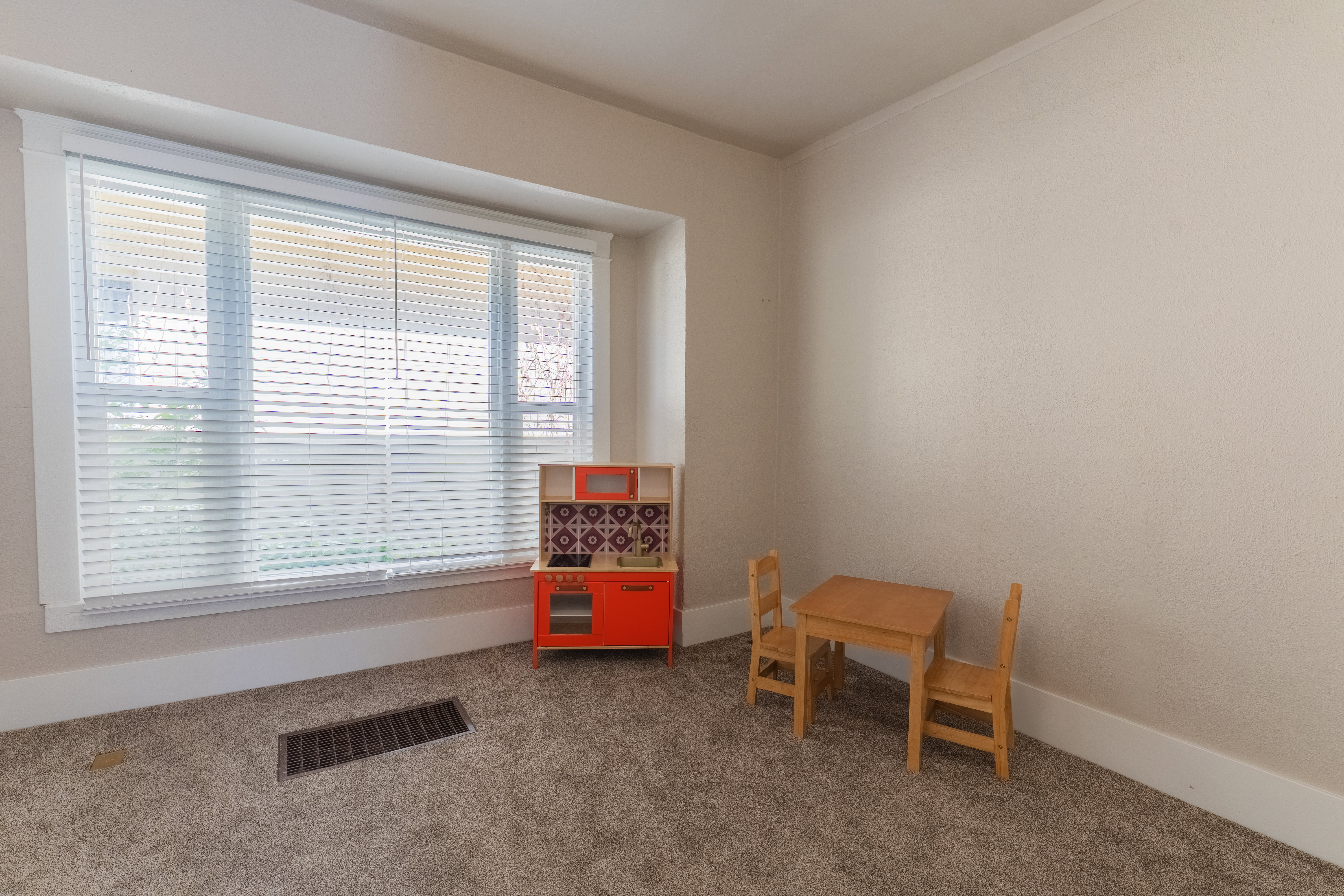 Room featuring a large window with white blinds, neutral-toned walls, and carpeted flooring
