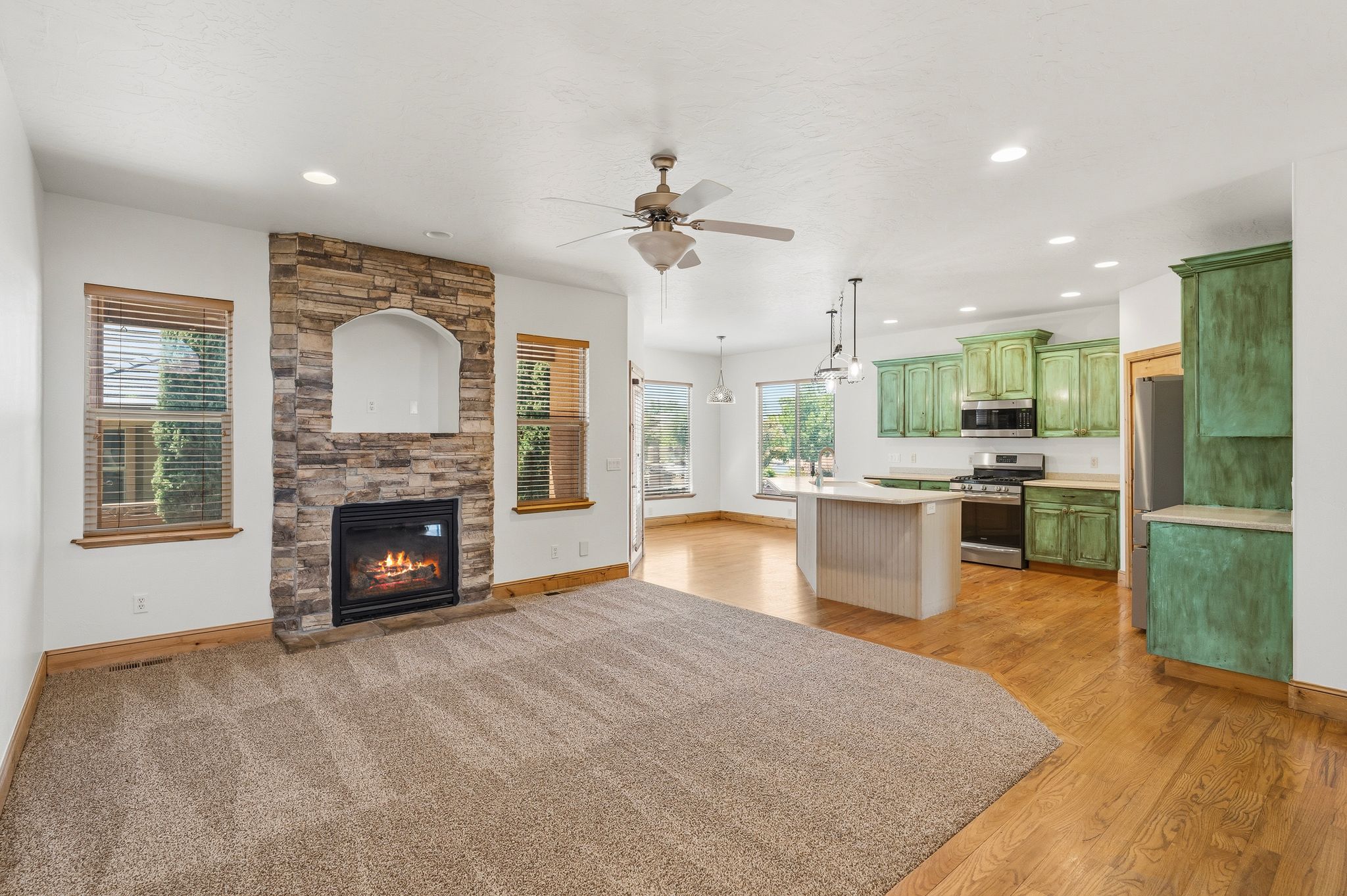 Living area featuring a stone-clad fireplace with an arched niche, carpeted flooring, and a ceiling fan