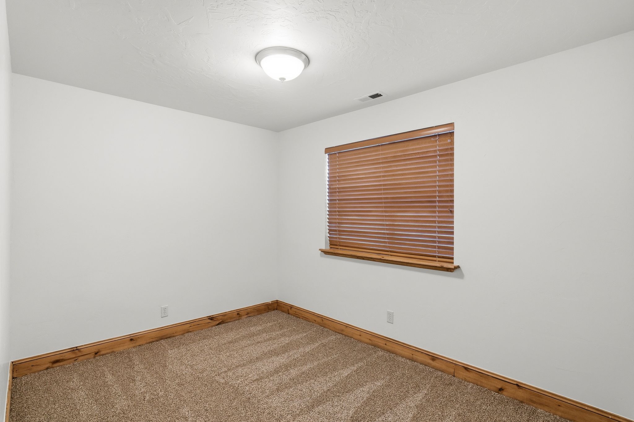 Neutral white walls with a window featuring wood-tone blinds and trim