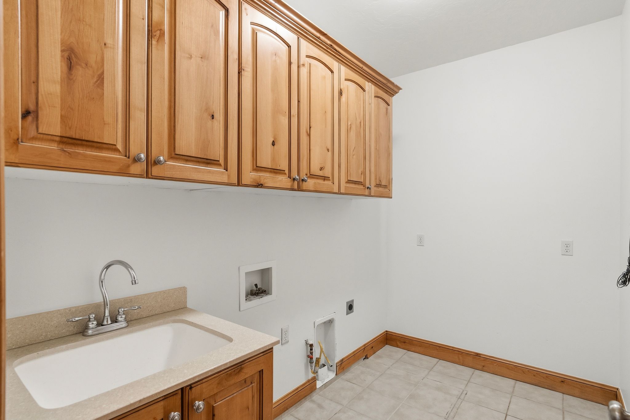 Utility room featuring extensive wood cabinetry, a utility sink with a stone-finish countertop, and tile flooring