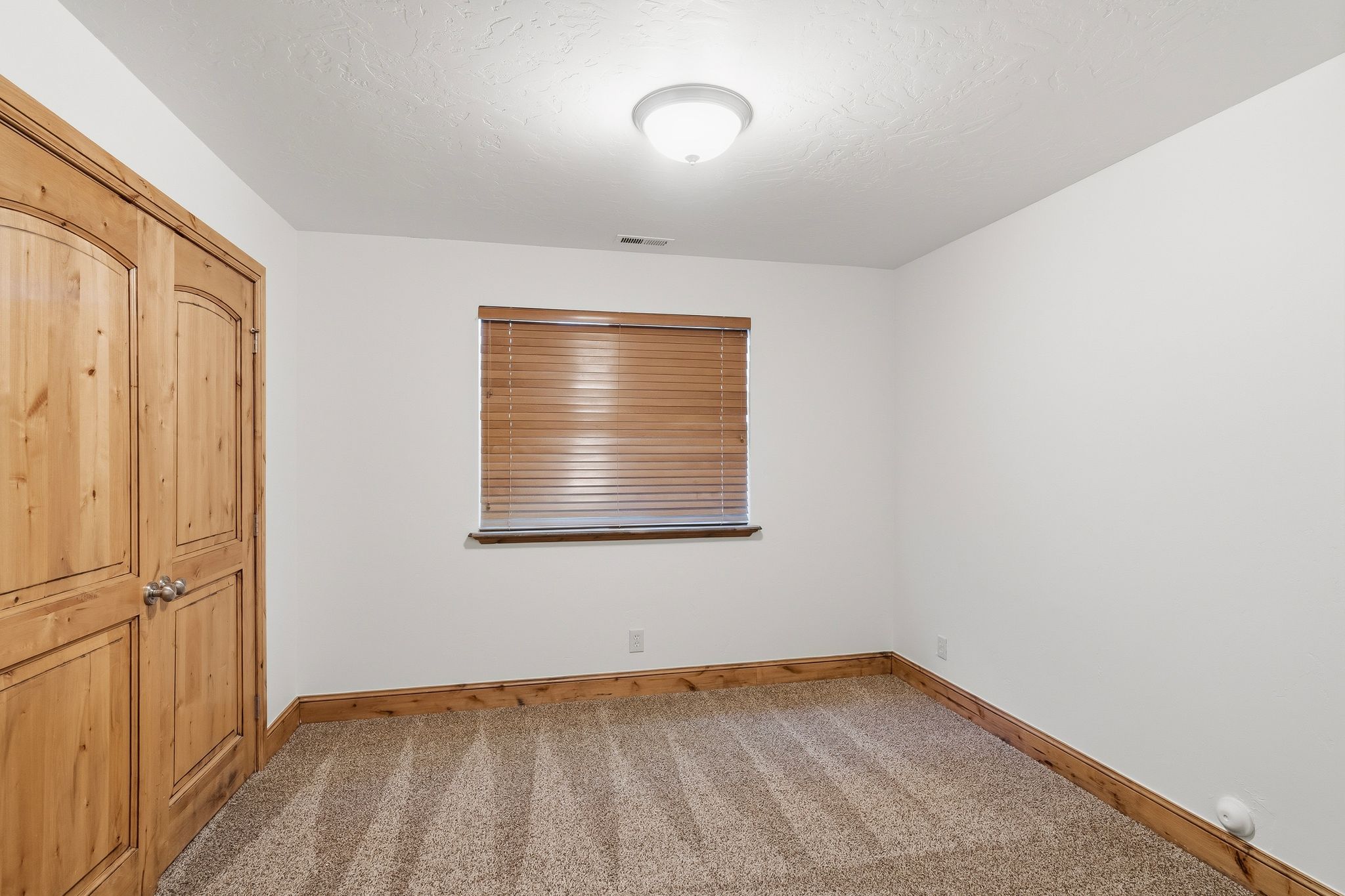 Bedroom featuring light wood double doors, a single window with wood blinds, and coordinated wood-finish baseboards