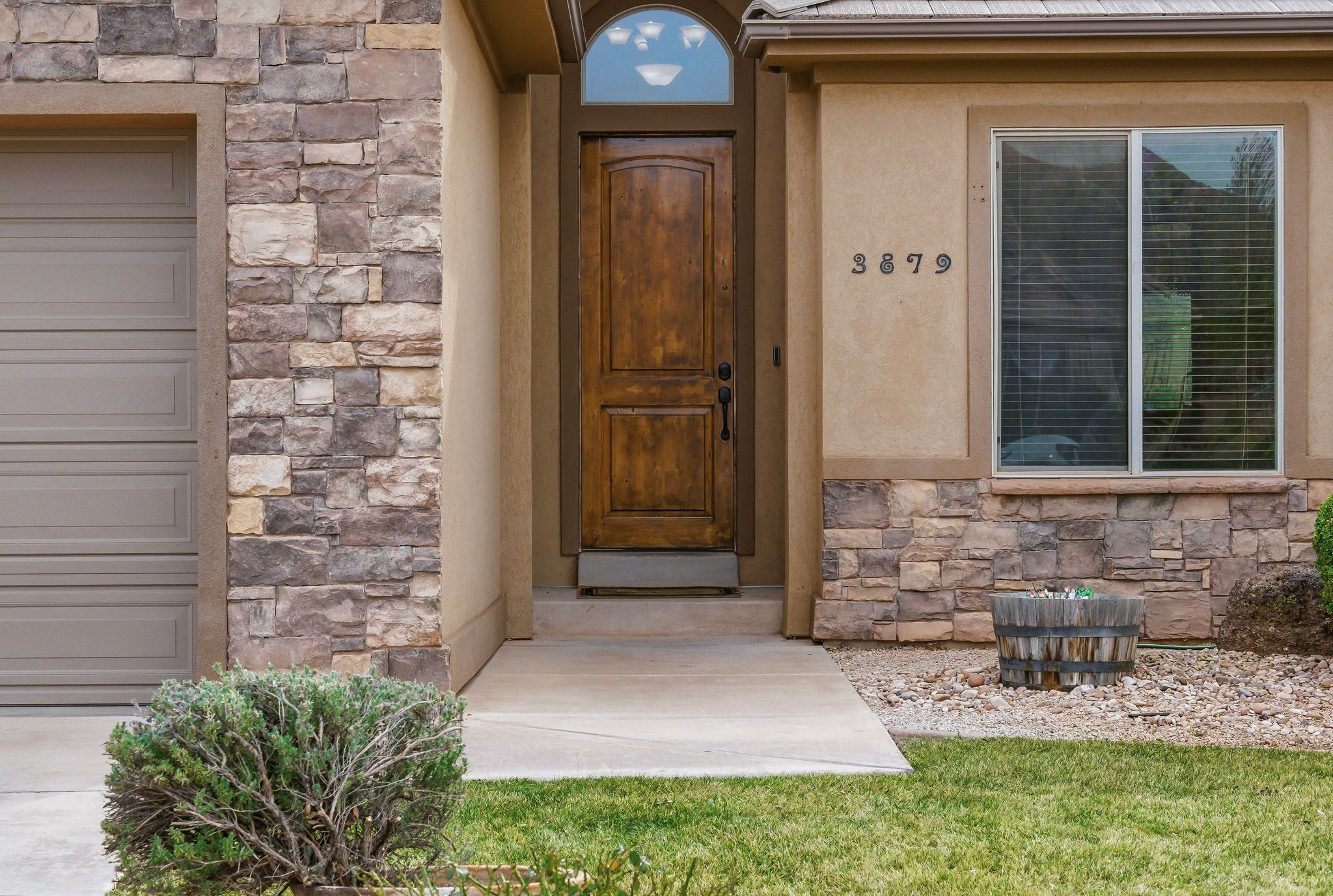Warm stucco exterior featuring stone veneer accents, a paneled wood-finish front door with an arched transom, and a concrete pathway