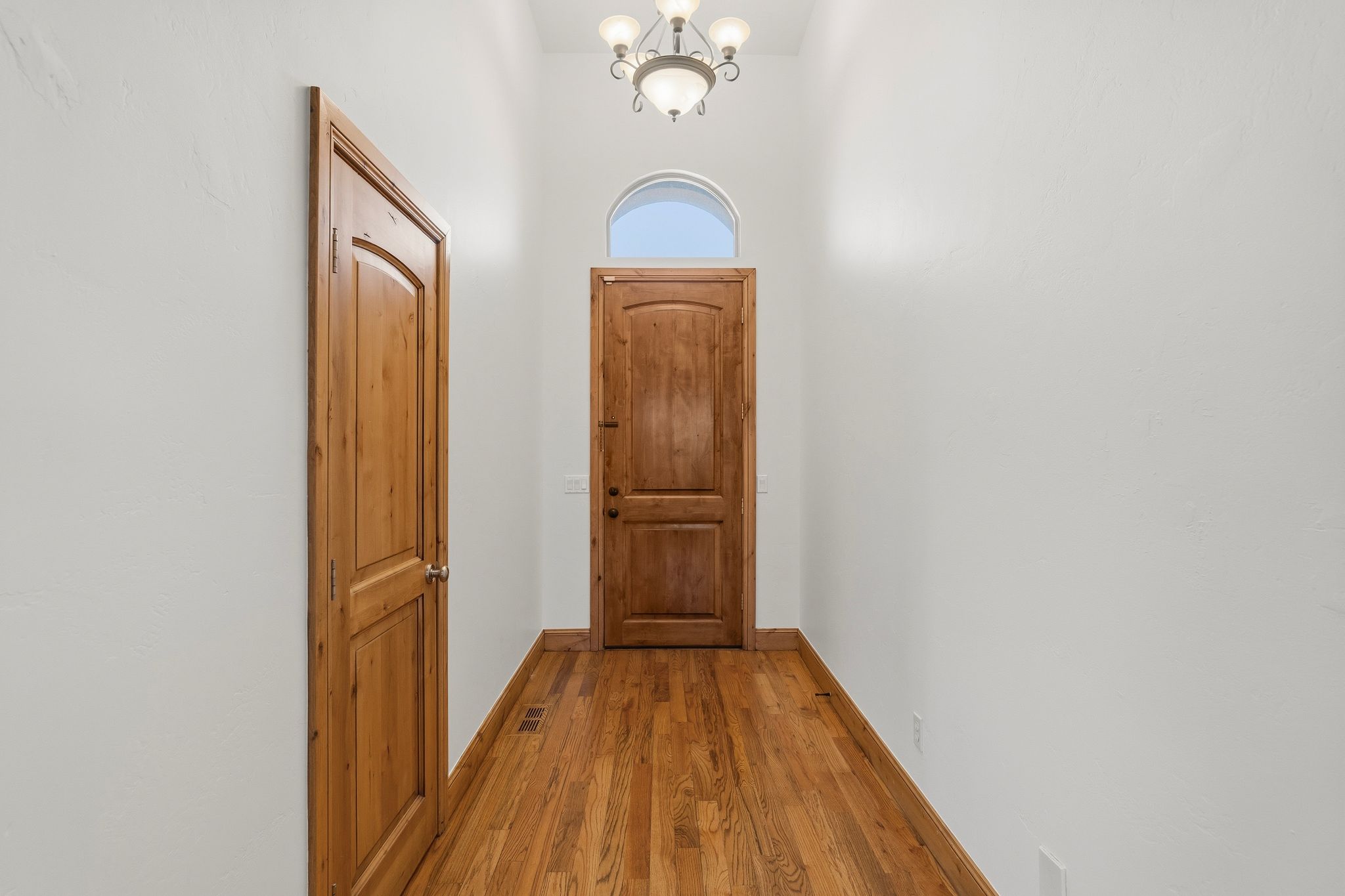 Entryway featuring hardwood flooring, a wood-paneled door, and a decorative light fixture