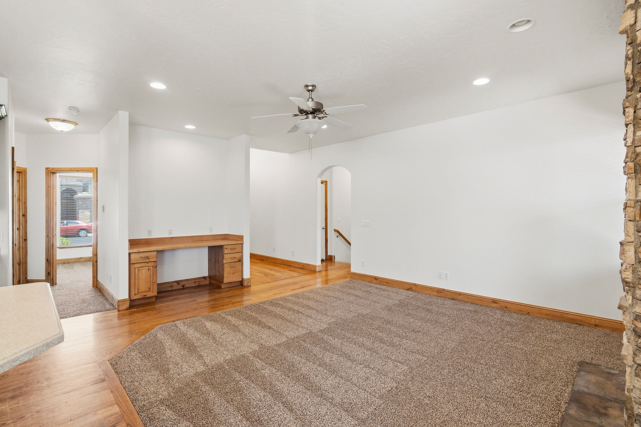 Spacious living area featuring a stone fireplace surround, wood-finish flooring, recessed lighting, and a built-in desk with cabinetry
