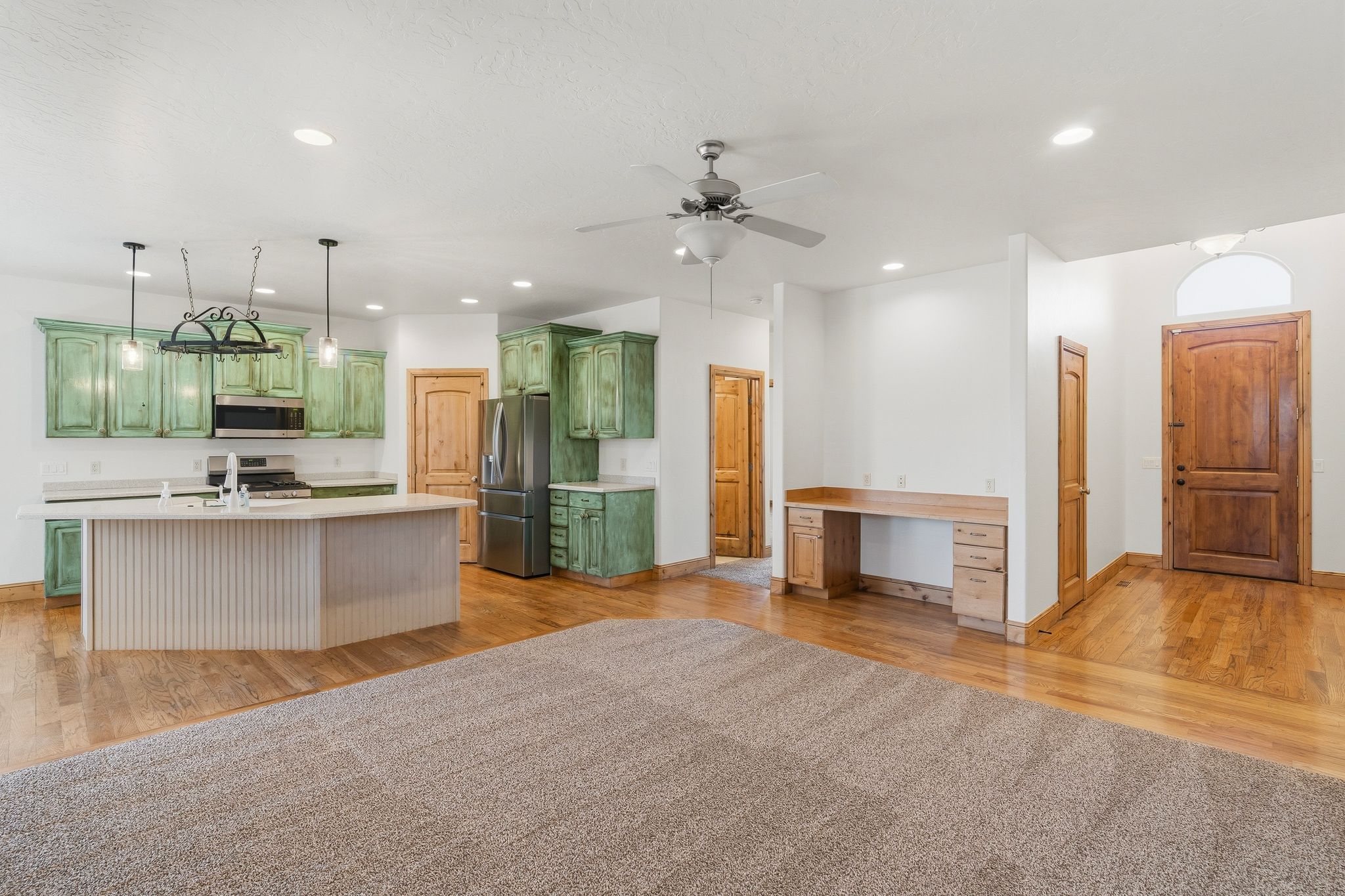 Open-concept living space featuring a kitchen with distressed green cabinetry, stainless steel appliances, and an island with a breakfast bar