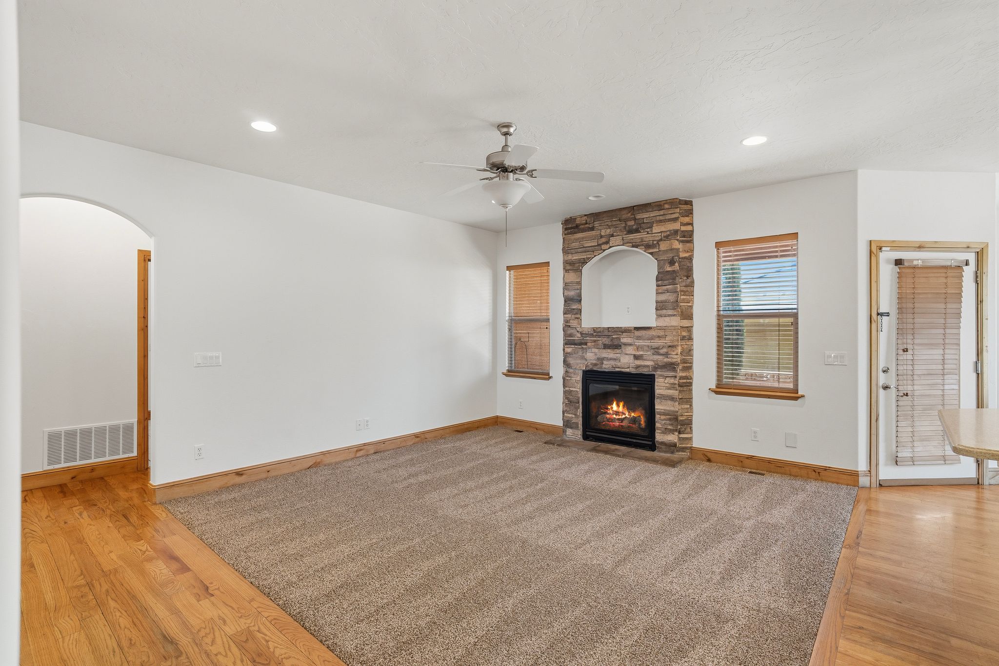 Living area featuring a floor-to-ceiling stone fireplace with an arched niche, recessed lighting, and a ceiling fan
