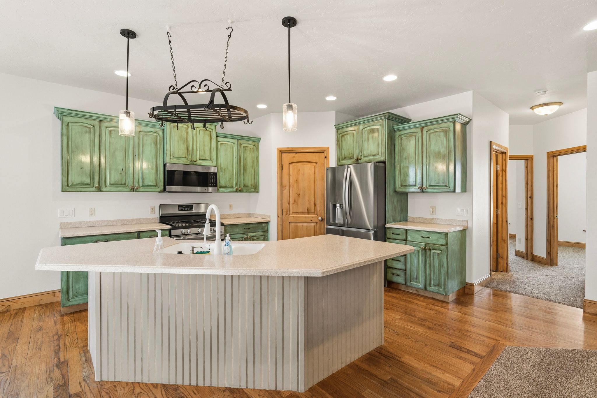 Kitchen featuring green distressed cabinetry, stainless steel appliances, a center island with bar seating, pendant lighting, and wood-finish flooring