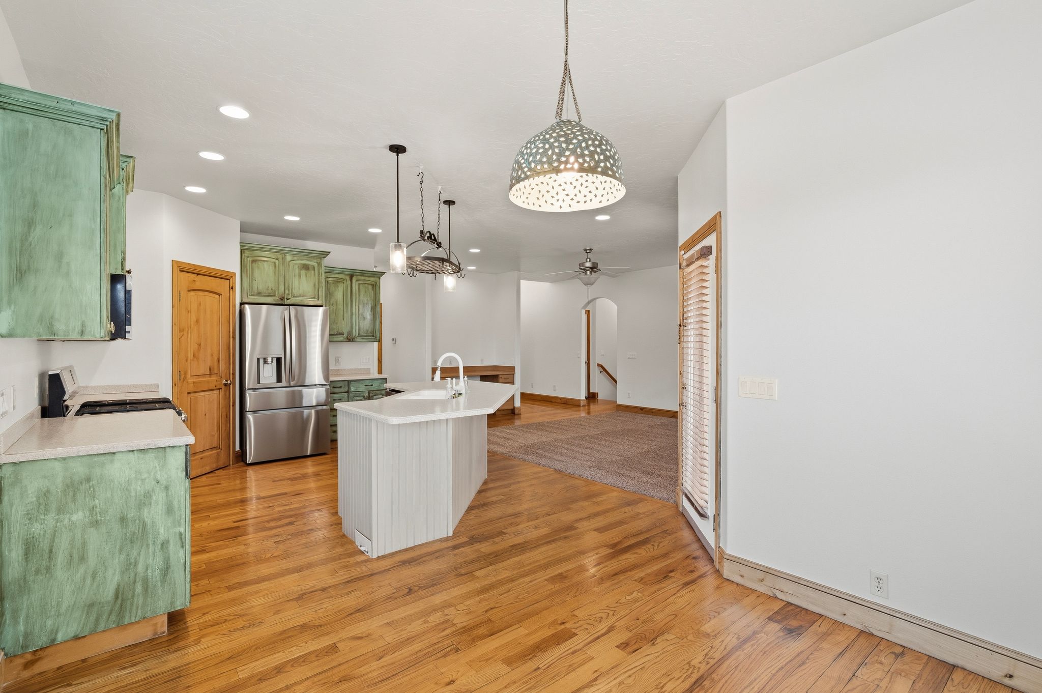 Open-concept kitchen featuring wood-finish flooring, light-toned countertops, and green-finished cabinetry
