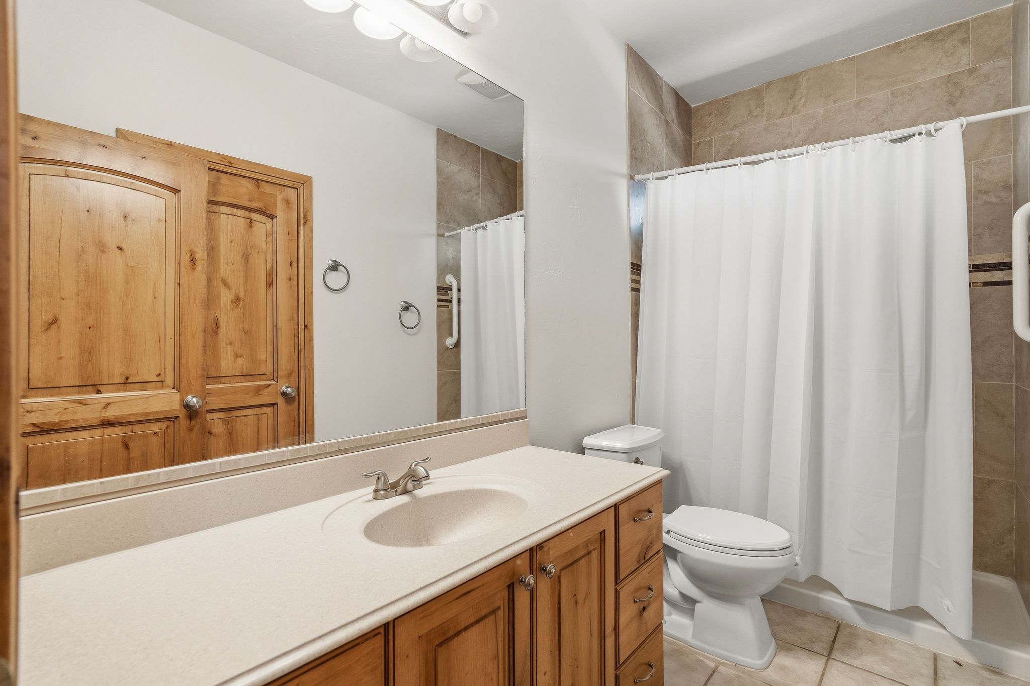 Bathroom with a light wood-finish vanity, integrated sink, and stone-finish countertop