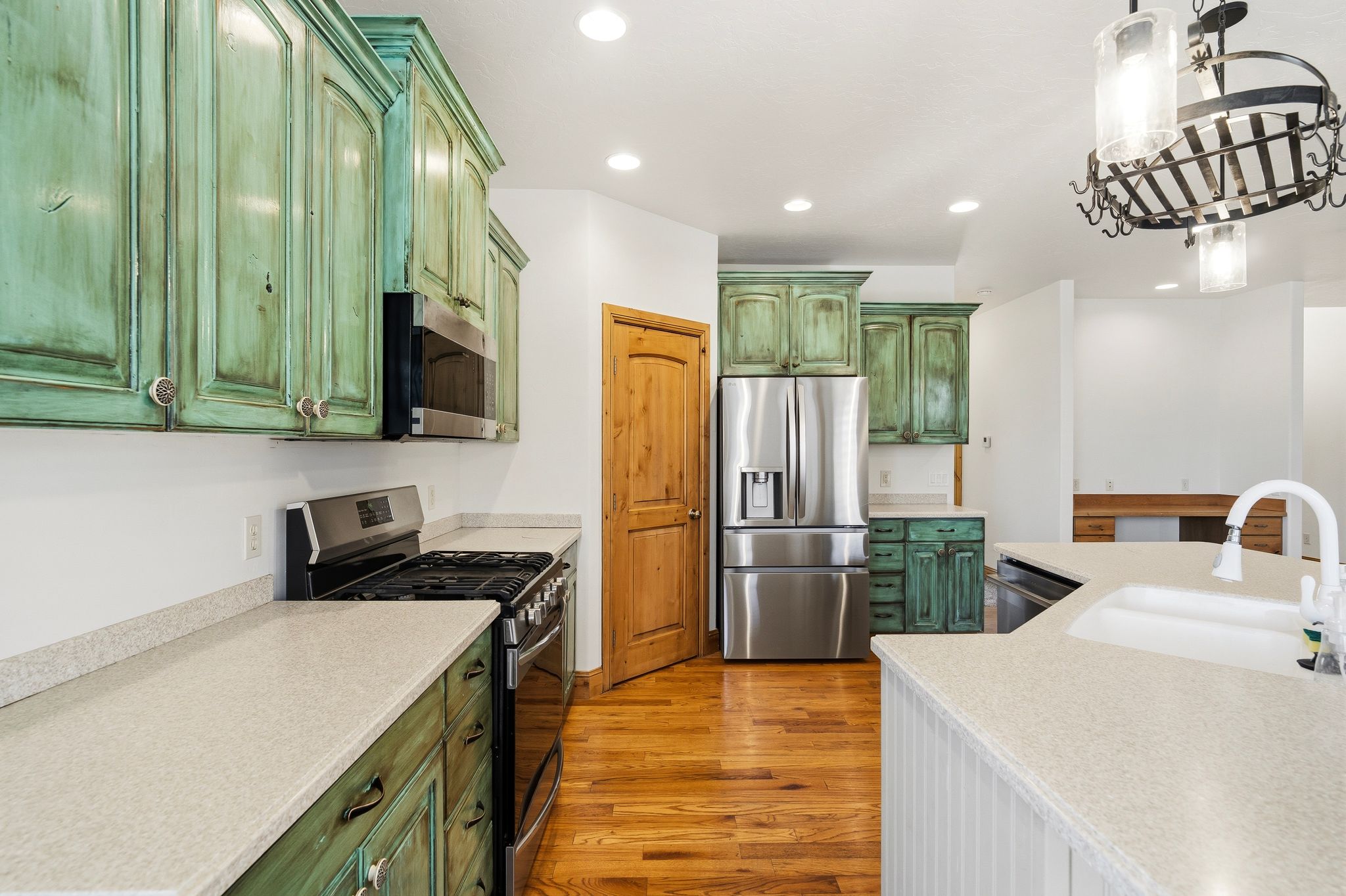 Kitchen featuring distressed green cabinetry, stainless steel appliances, light-toned countertops, hardwood flooring, and recessed lighting