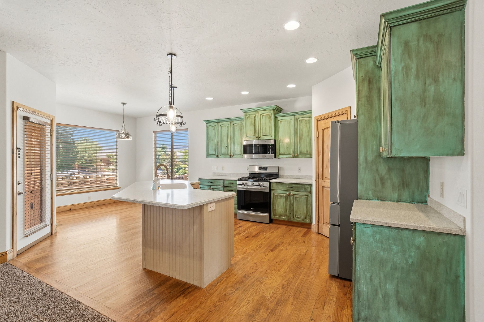 Open concept kitchen featuring an island with a built-in sink, stainless steel appliances, vibrant cabinetry, recessed lighting, and wood-finish flooring