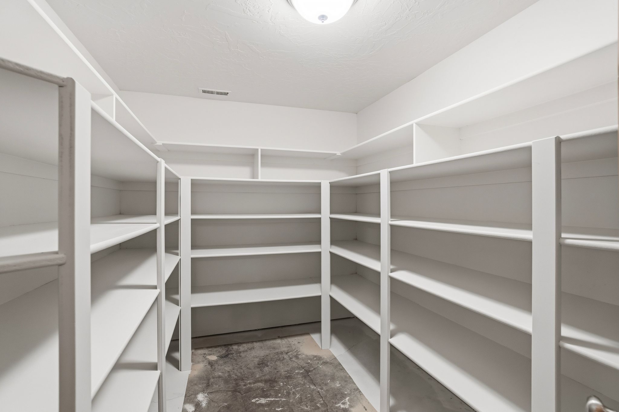 Expansive walk-in pantry featuring white built-in shelving, a flush mount ceiling light, and a textured ceiling