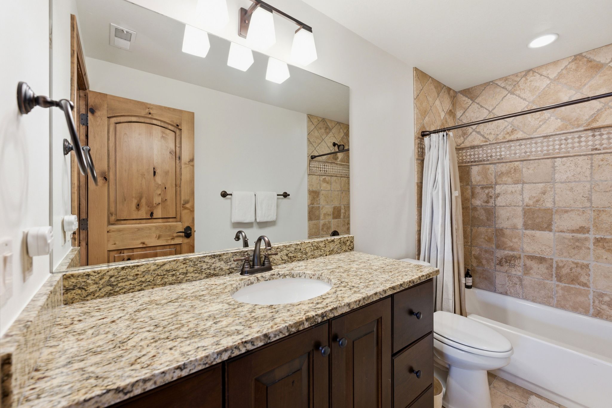 Bathroom featuring a single vanity with stone countertop, dark wood cabinetry, and an undermount sink