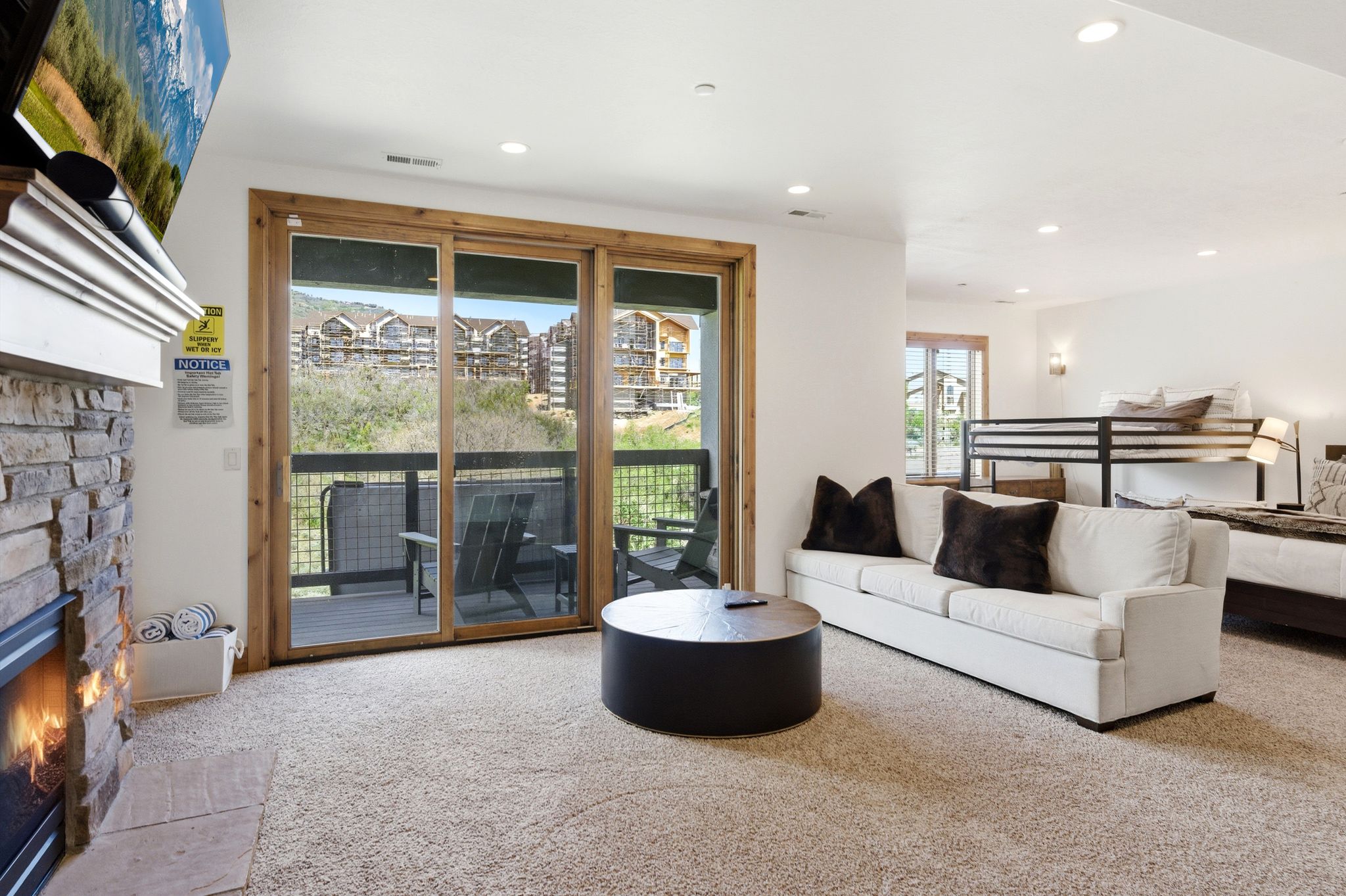 Living area featuring a stone-clad fireplace with a classic mantel, glass sliding doors opening to a private balcony, recessed lighting, and soft carpet flooring