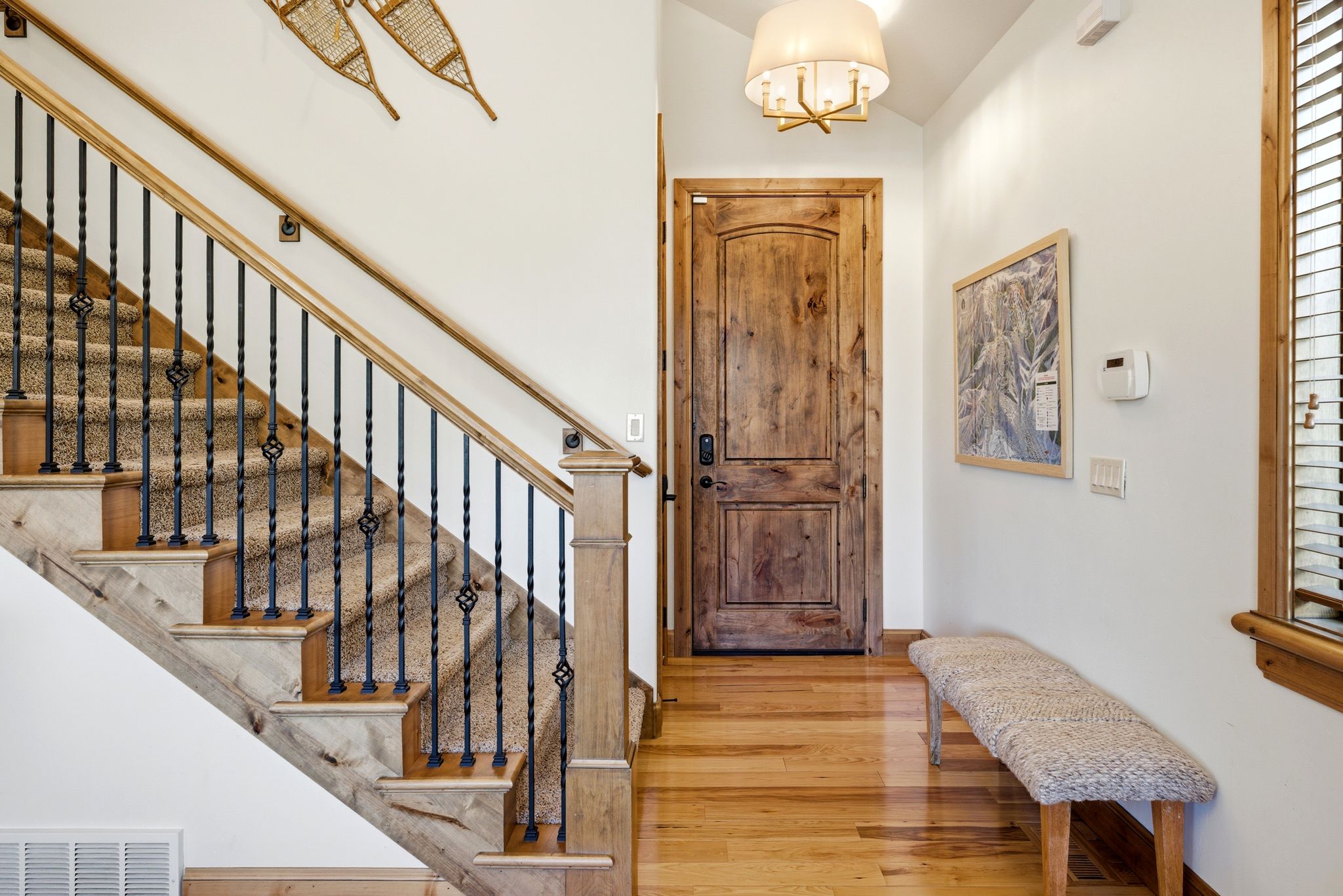 Entryway featuring a solid wood door, hardwood flooring, and a staircase with wrought iron balusters and carpeted treads