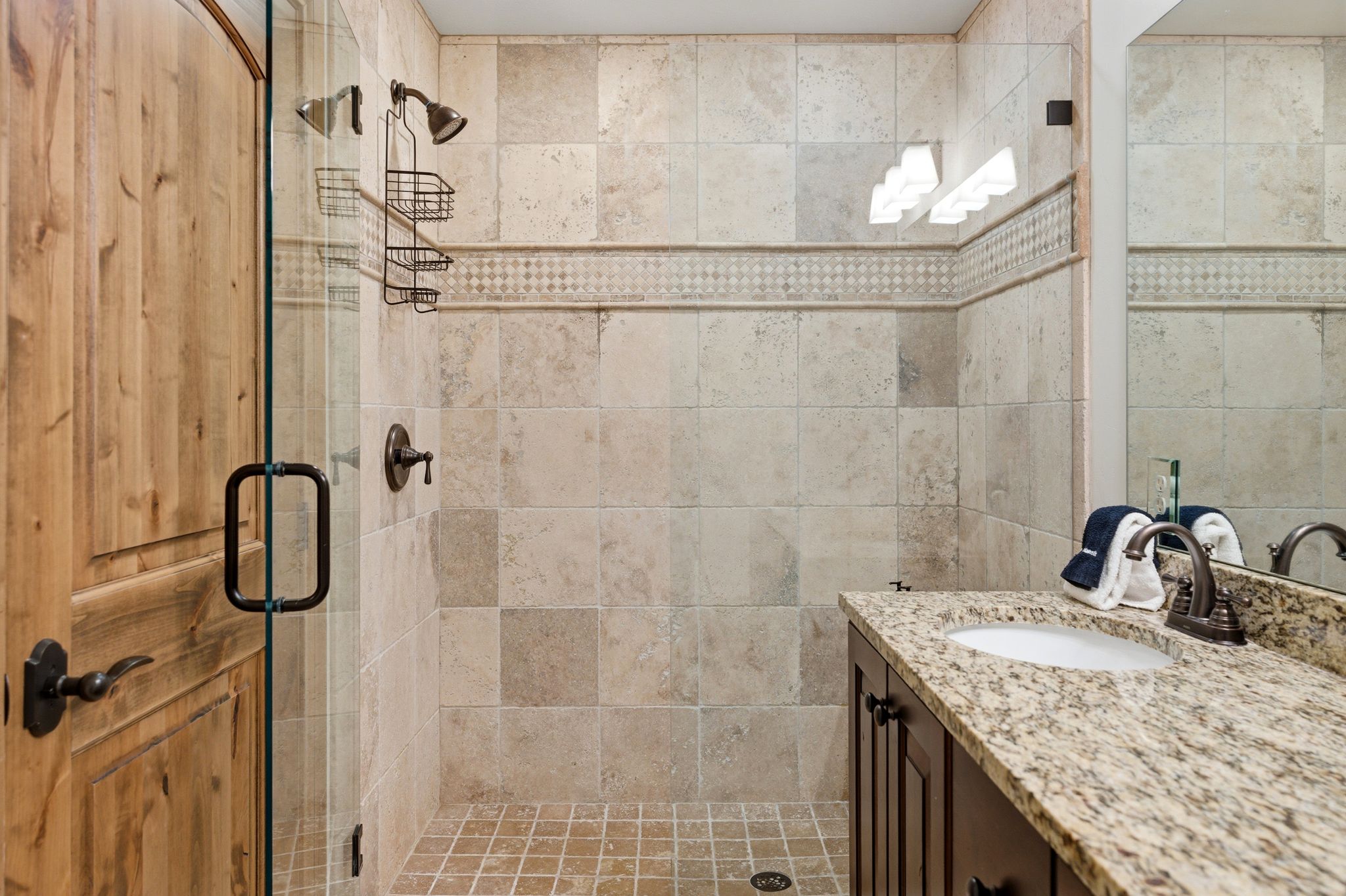 Spacious bathroom featuring a glass-enclosed shower with tiled walls and a decorative accent band