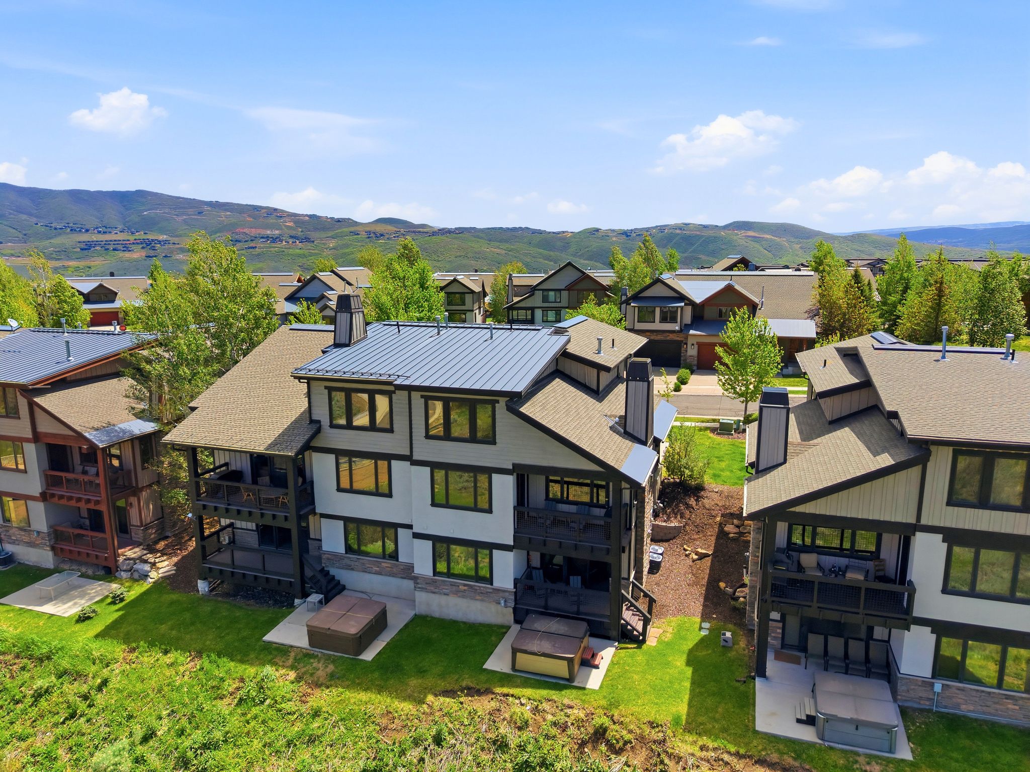Modern multi-story property featuring a metal roof section, multiple balconies, and an exterior hot tub