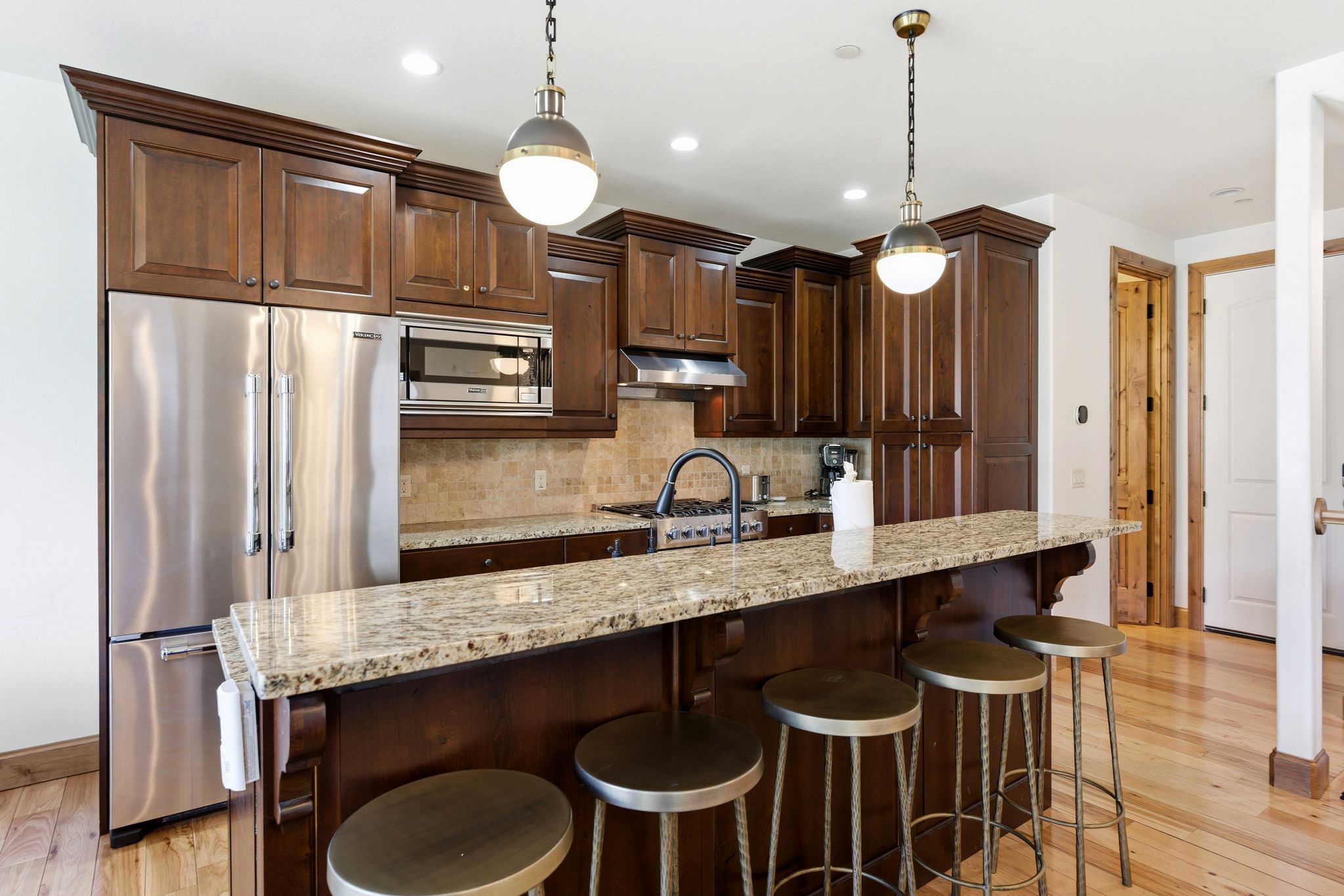 Kitchen featuring dark wood cabinetry, stainless steel appliances, a tile backsplash, and a light-toned granite countertop island with pendant lighting