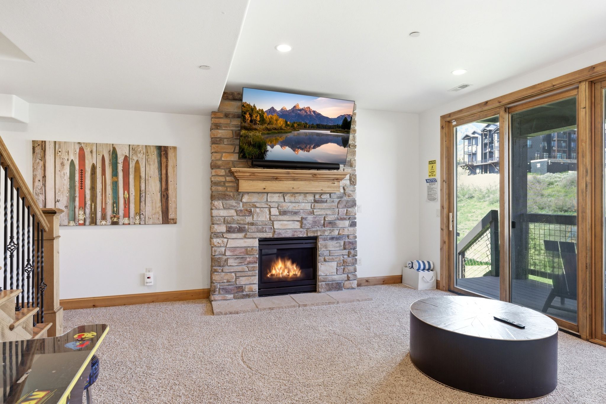 Stacked stone fireplace with a wood mantel, built-in television, and recessed lighting