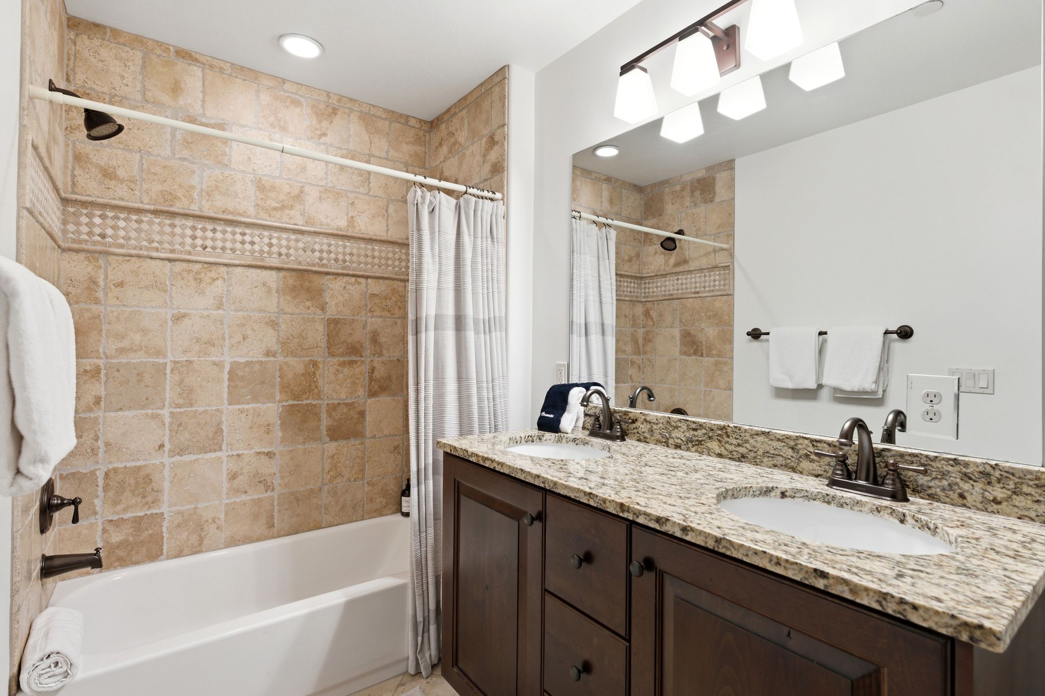 Bathroom featuring a dual-sink vanity with a light-colored stone countertop, dark wood-finish cabinetry, and a full-width mirror