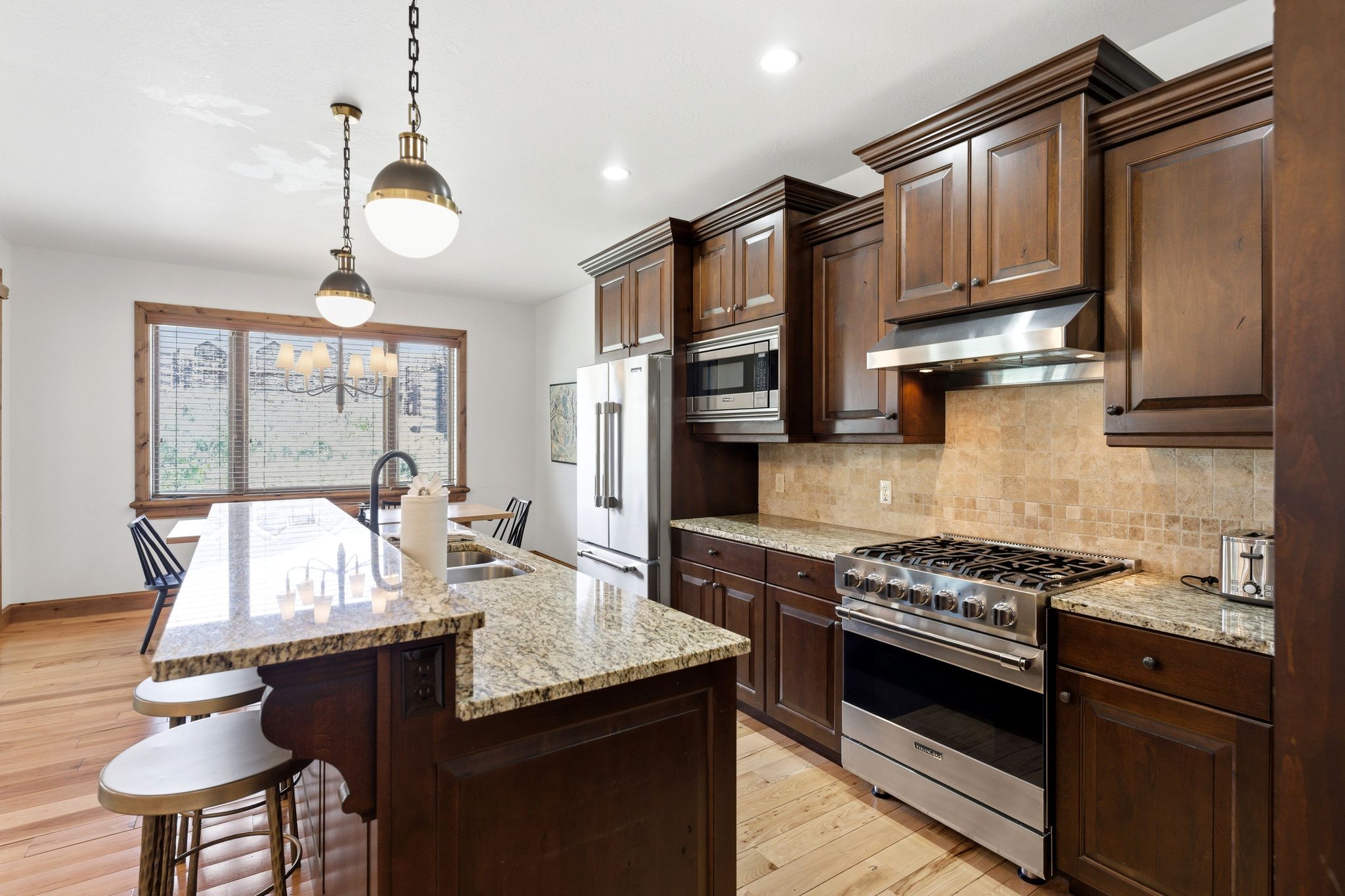 Kitchen featuring wood-finish flooring, dark wood cabinetry, granite countertops, and stainless steel appliances