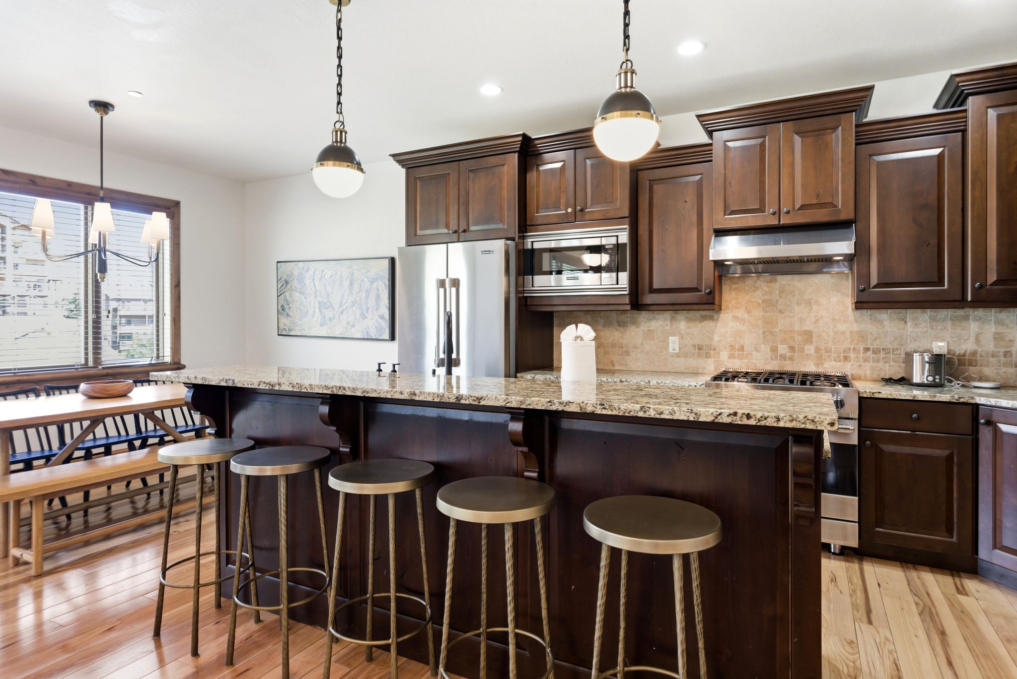 Kitchen featuring a large central island with a light-colored granite countertop, dark wood cabinetry, stainless steel appliances, a tile backsplash, and light wood-finish flooring