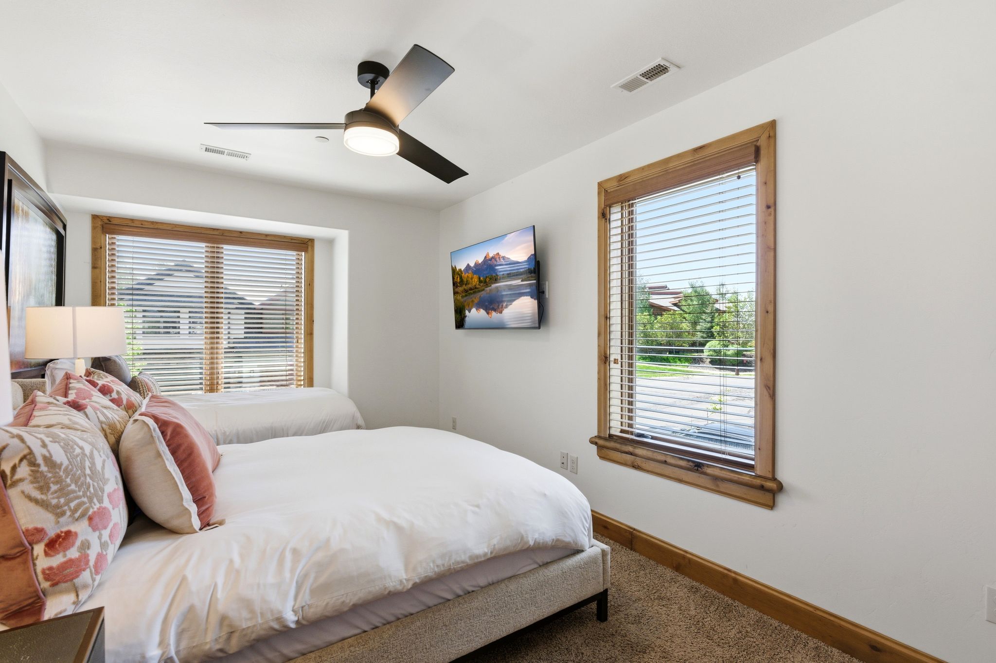 Bedroom featuring a ceiling fan with integrated lighting, wood-trimmed windows with blinds, and neutral carpet flooring