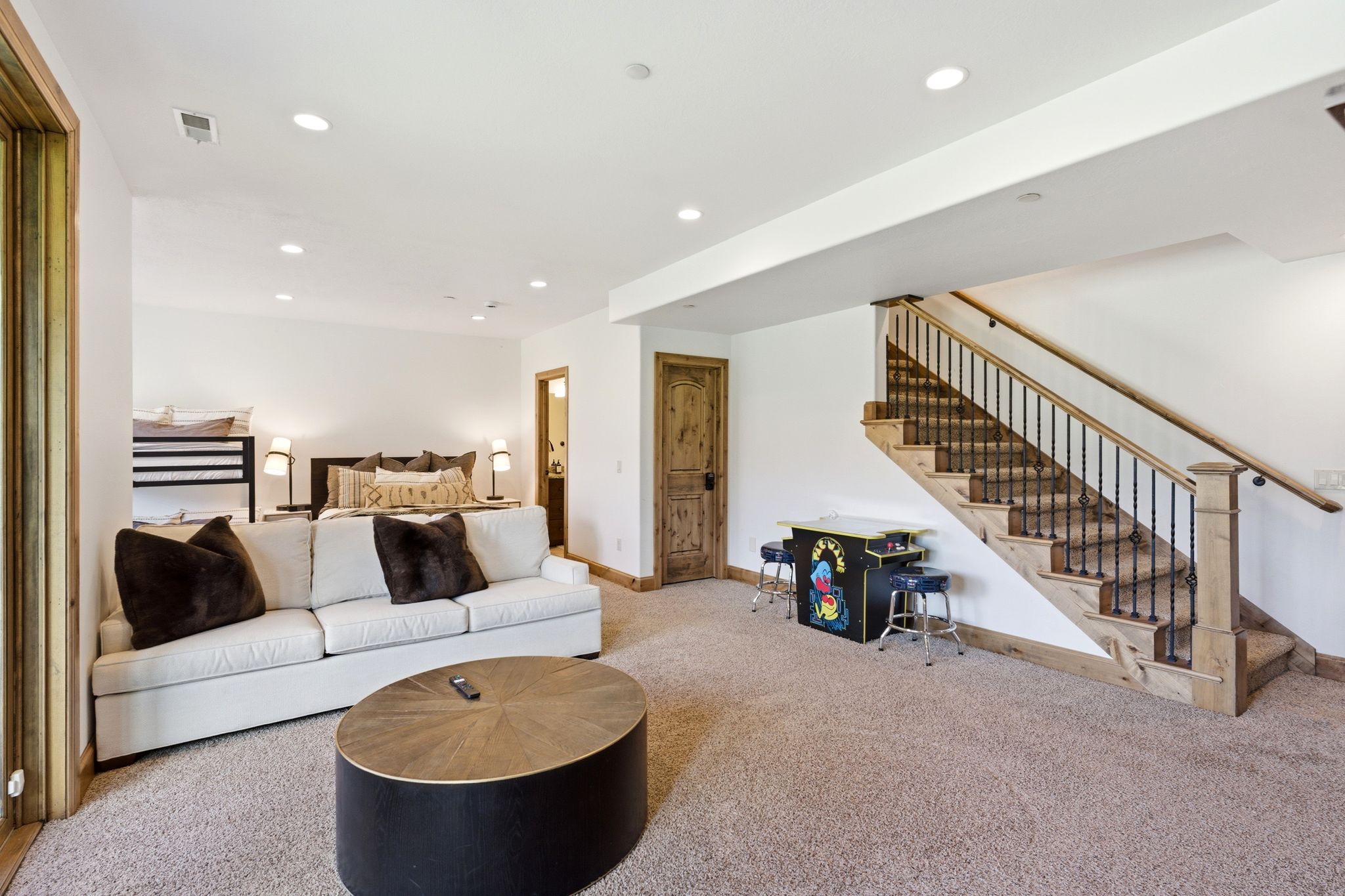 Carpeted recreation area featuring a wood staircase with wrought iron balusters, recessed lighting, and a wood-paneled door