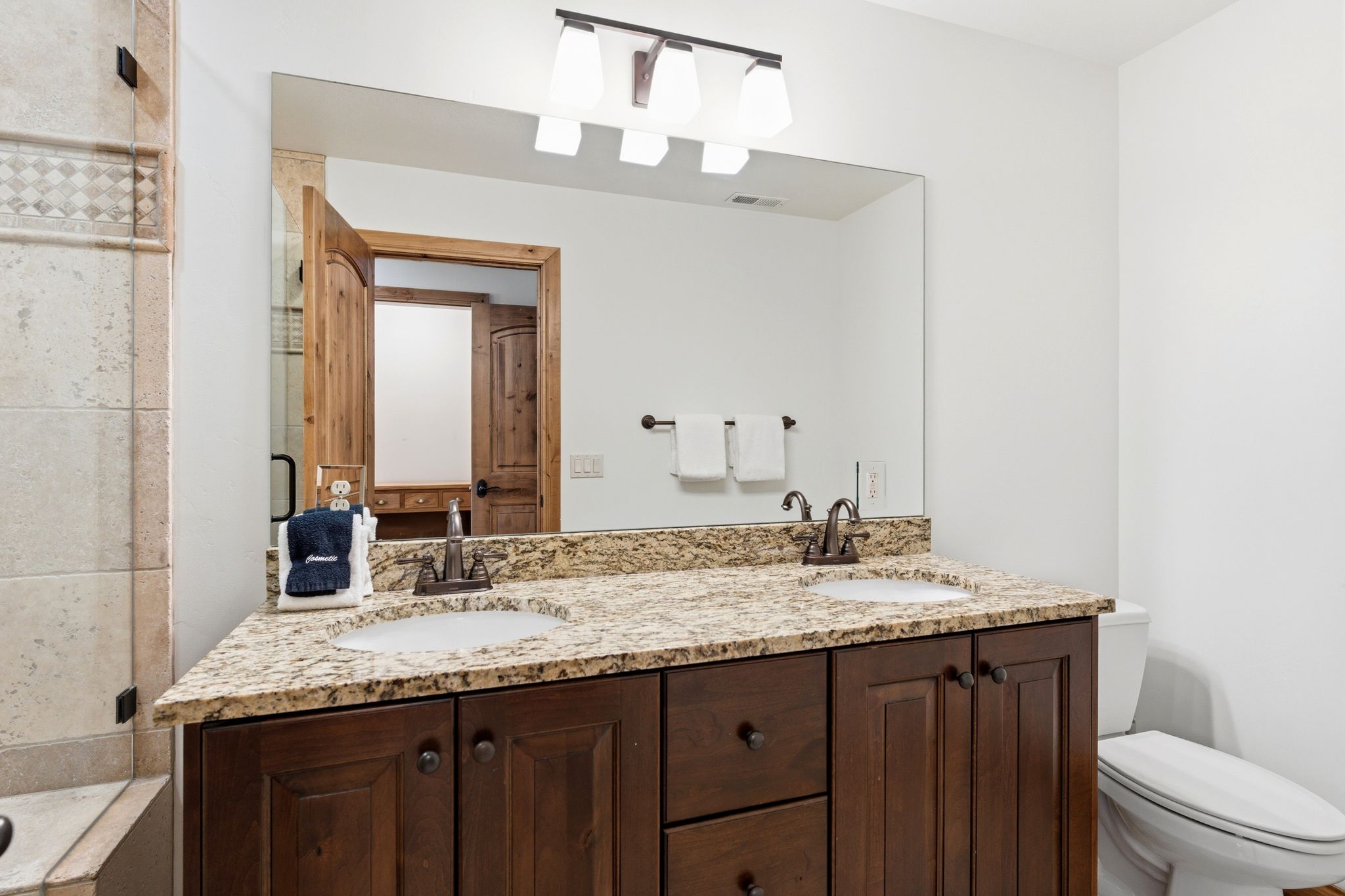 Bathroom vanity featuring a granite countertop with two integrated sinks, dark wood-finish cabinetry, and brushed bronze fixtures
