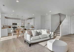 Open-concept living space featuring wood-finish flooring, a contemporary kitchen with white cabinetry and stainless steel appliances, recessed lighting, pendant lighting, and a carpeted staircase. This picture is of another home