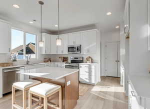 Bright kitchen featuring white cabinetry, stainless steel appliances, a white quartz island with wood-finish paneling, recessed lighting, and wood-finish flooring. This picture is of another home.