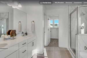 Bathroom featuring a spacious dual vanity with white cabinetry and integrated sinks, a walk-in shower with glass enclosure and tiled walls, and large format tile flooring. This picture is of another home