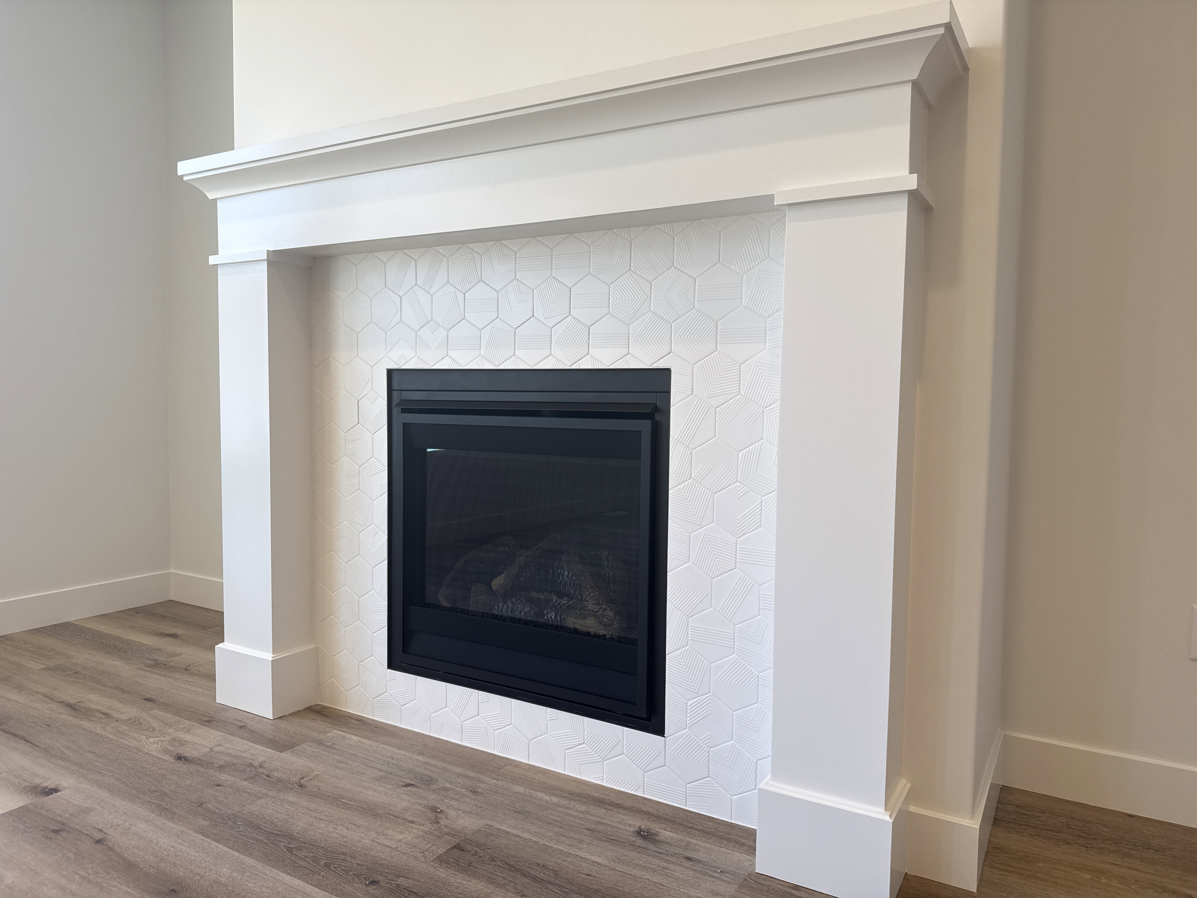 Modern fireplace with a white mantel and surround, featuring a white hexagonal tile hearth, a black-framed insert, and wood-finish flooring