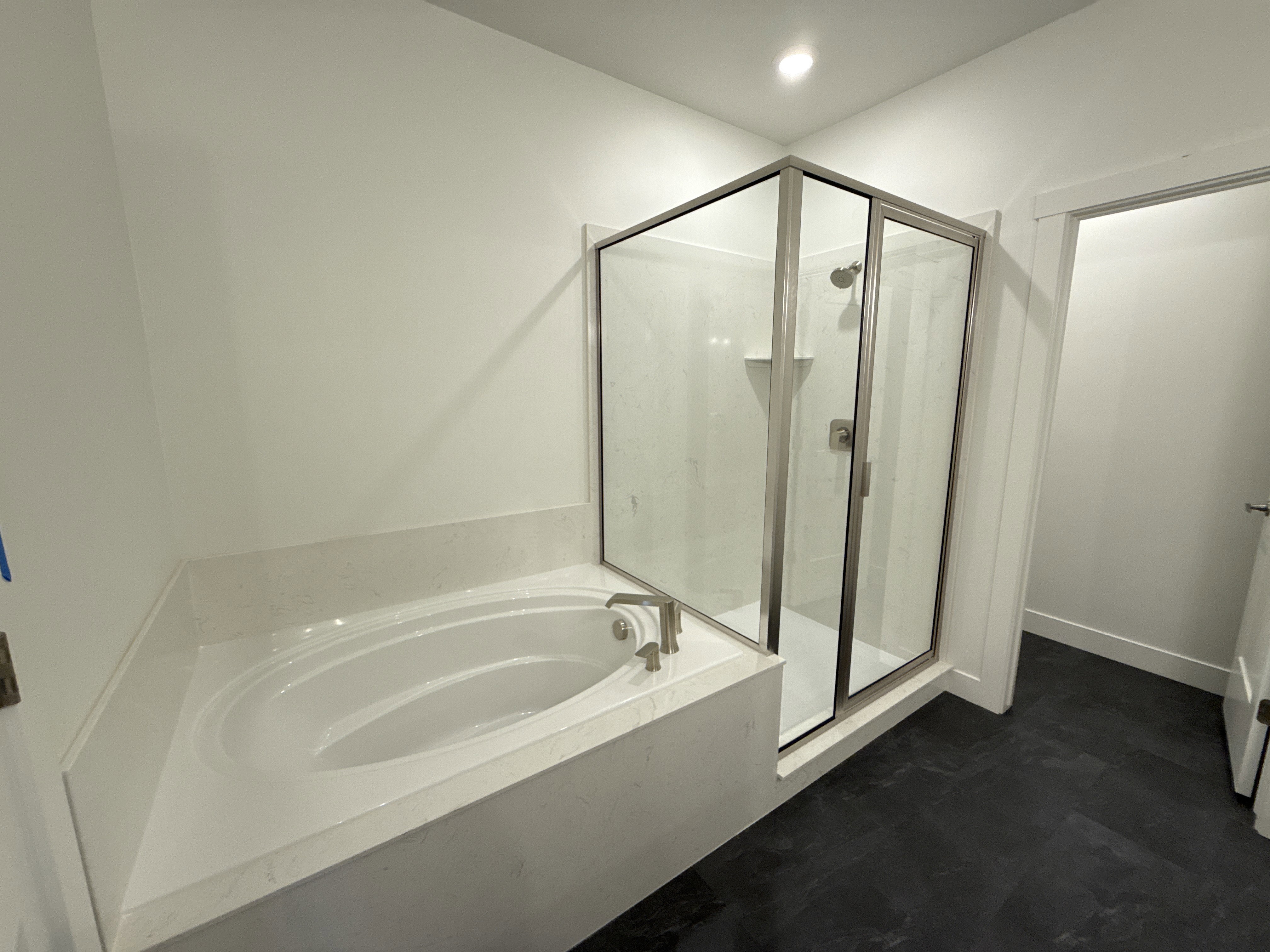 Corner soaking tub with a surrounding light-toned countertop, brushed nickel fixtures, and a glass-enclosed shower with a built-in shelf