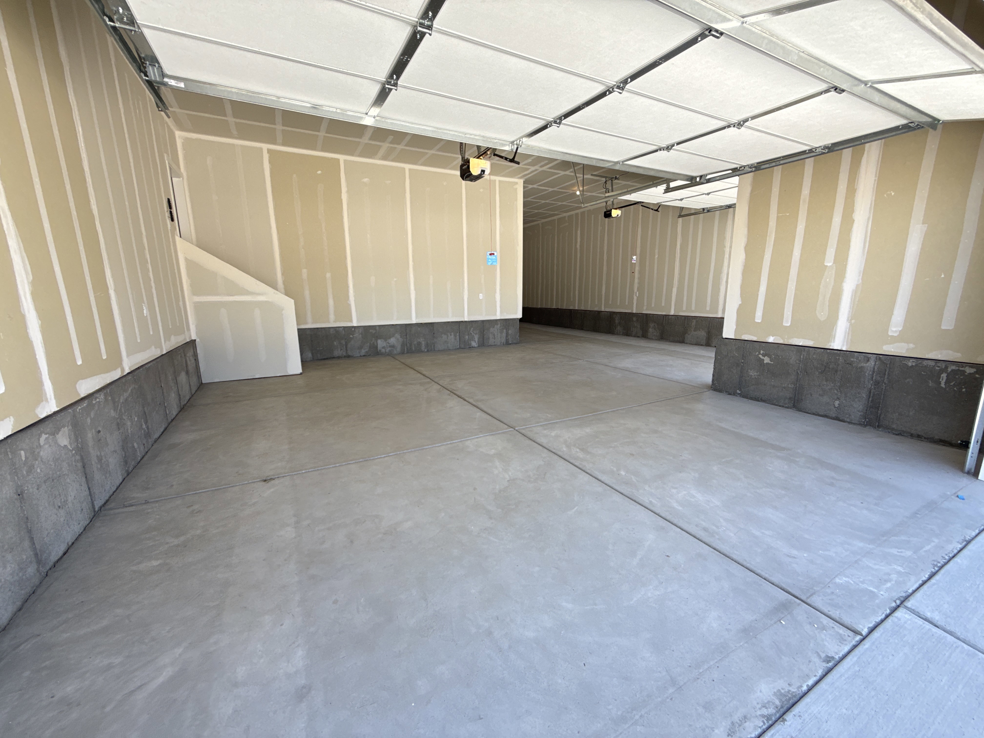 Spacious garage featuring concrete flooring, unpainted drywall walls, and an exposed ceiling with automatic door openers