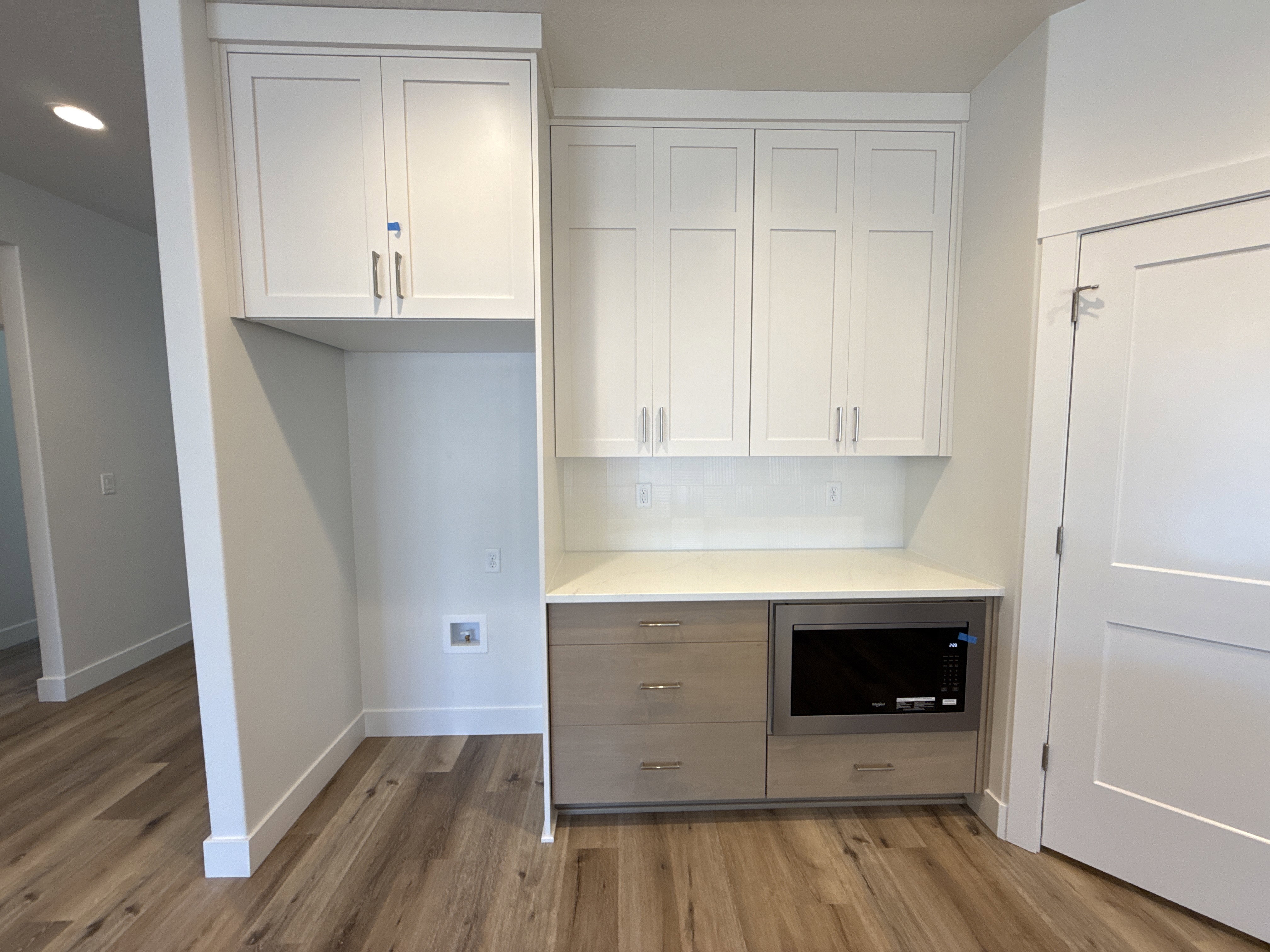 Built-in appliance cabinet featuring white shaker-style cabinetry, a light-toned countertop, and a stainless steel drawer microwave