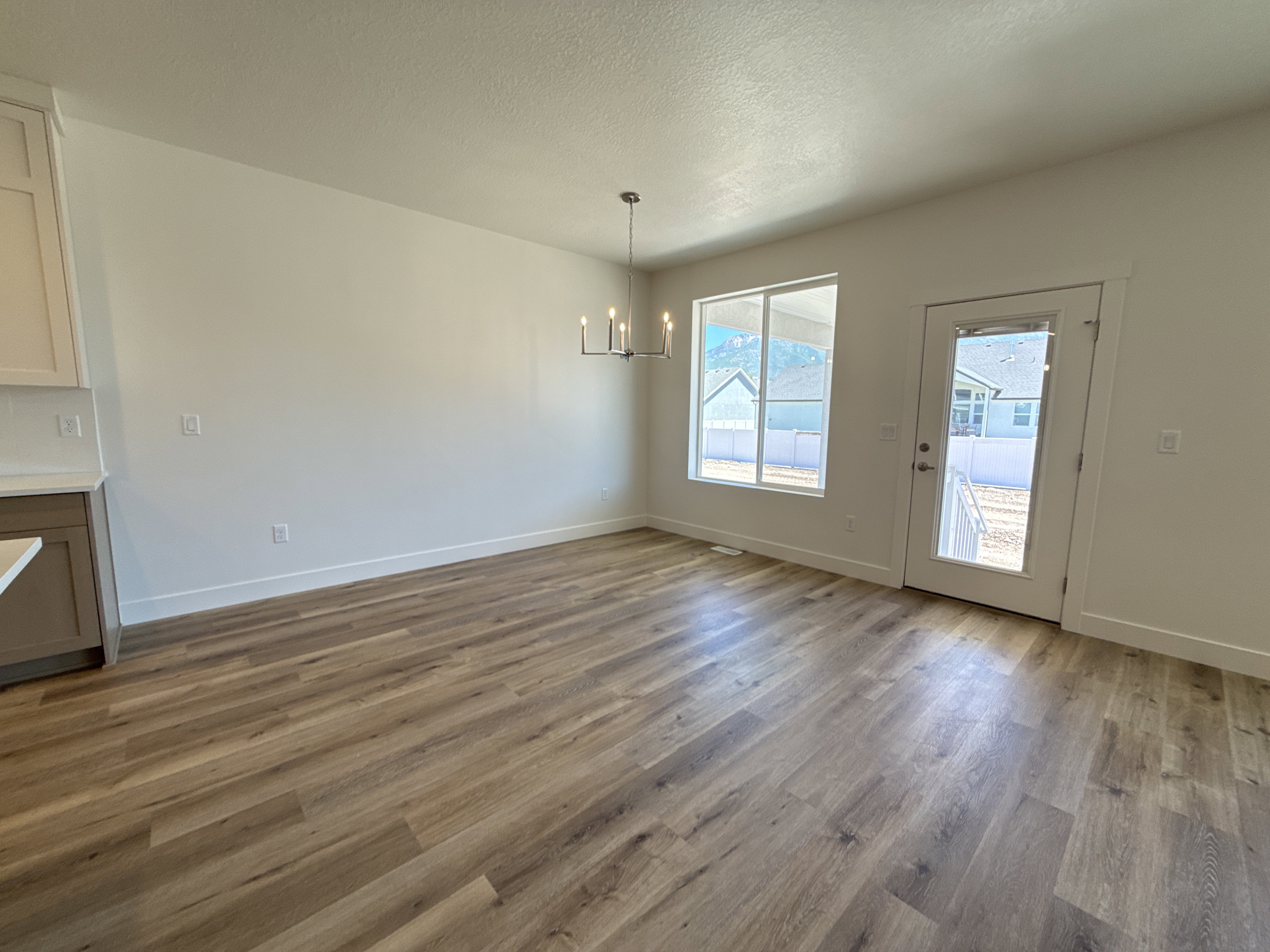 Spacious room featuring wood-finish flooring, white walls, and a contemporary chandelier
