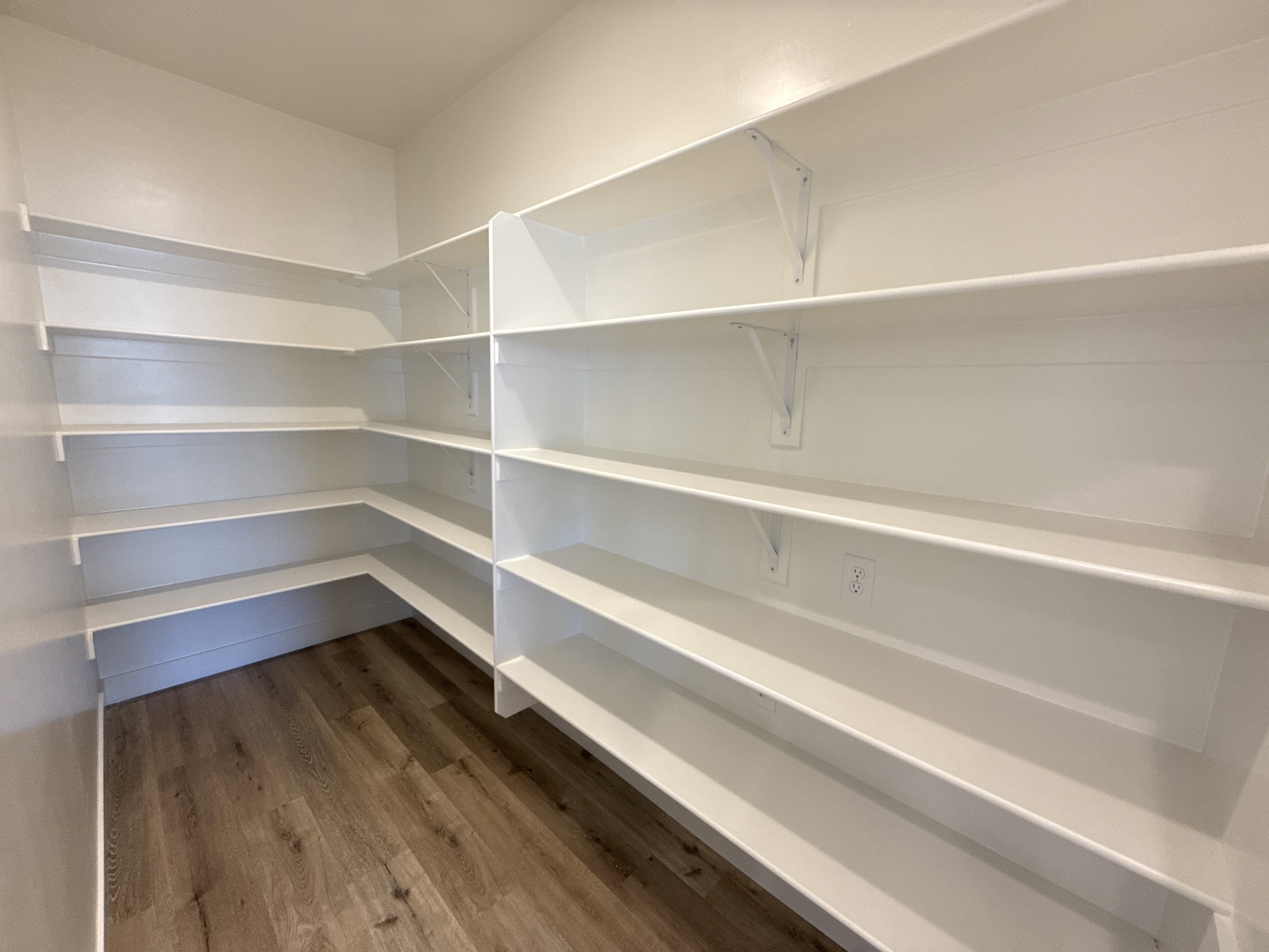 Corner pantry featuring extensive white shelving, wood-finish flooring, and electrical outlets